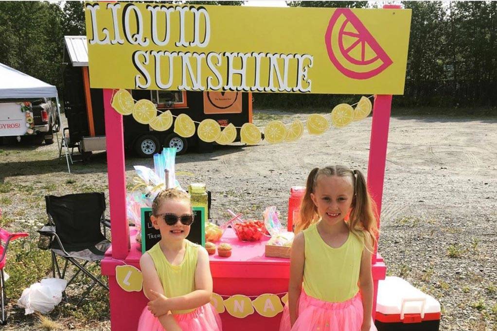 Ava McCaughey, left, and Zoey Stone, right, smile for the camera in front of their lemonade stand on Binkley Street during Lemonade Day in Soldotna, Alaska on June 29, 2019. (Photo courtesy Taylor Cochran)
