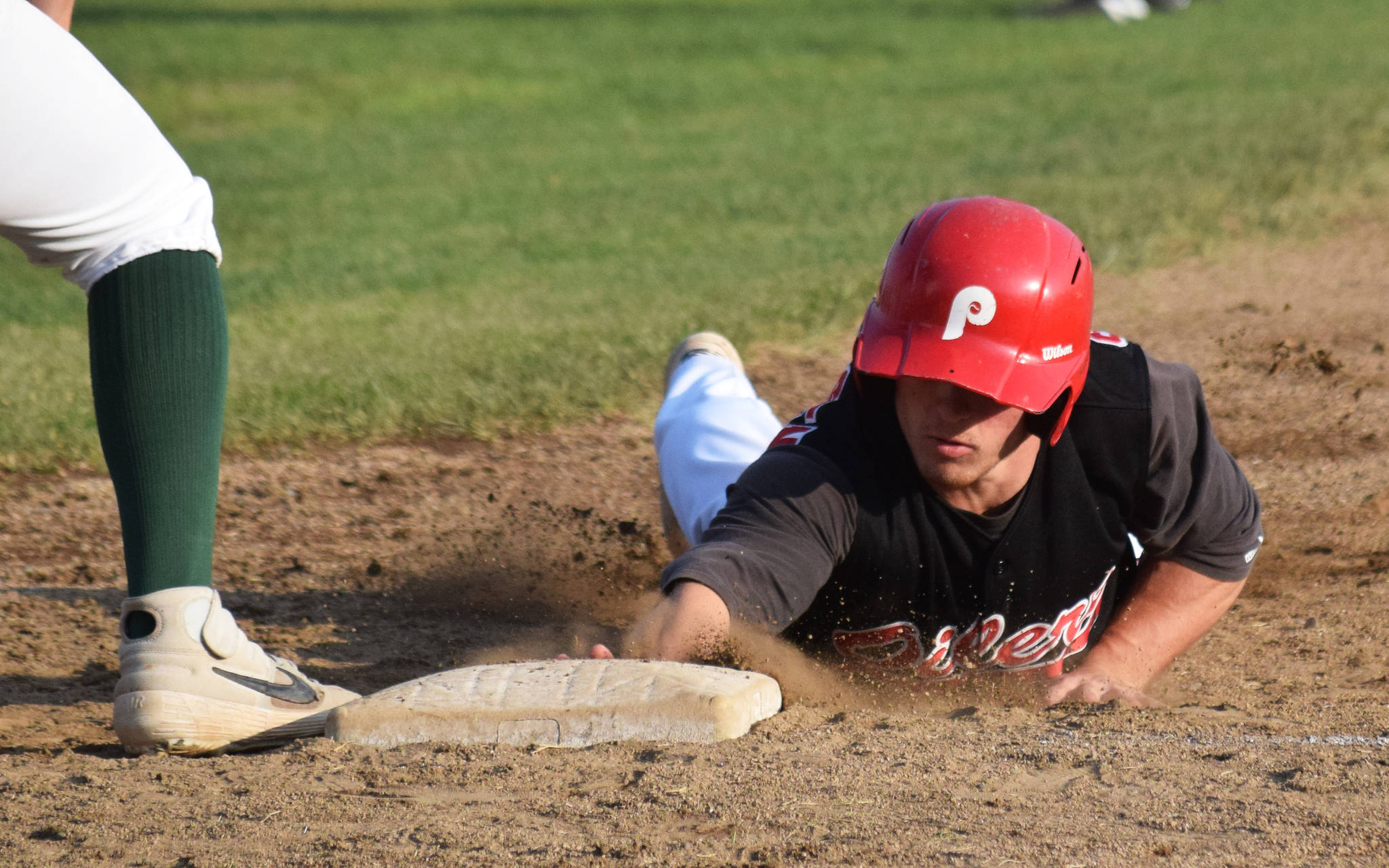 Peninsula Oilers baserunner Paul Steffensen tags first base to avoid the glove of Mat-Su Miners first baseman Drew Williamson Friday at Coral Seymour Memorial Park in Kenai. (Photo by Joey Klecka/Peninsula Clarion)