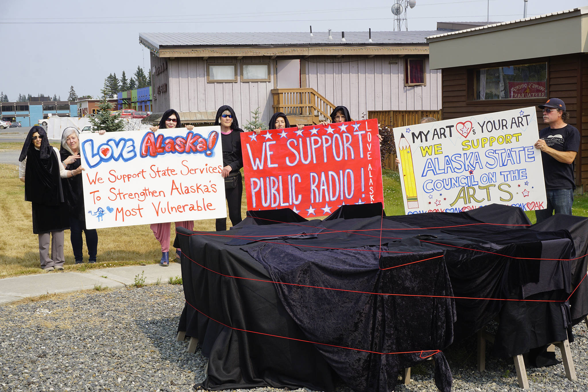 People draped in black hold signs on July 9, 2019, by Sean Derry’s public art sculpture in Homer, Alaska, as part of a statewide art intervention to protest Gov. Mike Dunleavy’s veto of a $2.8 million state appropriation to the Alaska State Council on the Arts. They also supported a general override of Dunleavy’s vetoes that will affect funding for the University of Alaska, public radio and other programs. Derry’s sculpture was commissioned as a 1% for art project associated with the remodeling of Pioneer Hall at the Kachemak Bay Campus, Kenai Peninsula College, University of Alaska. The protest was not sanctioned by the college. (Photo by Michael Armstrong/Homer News)