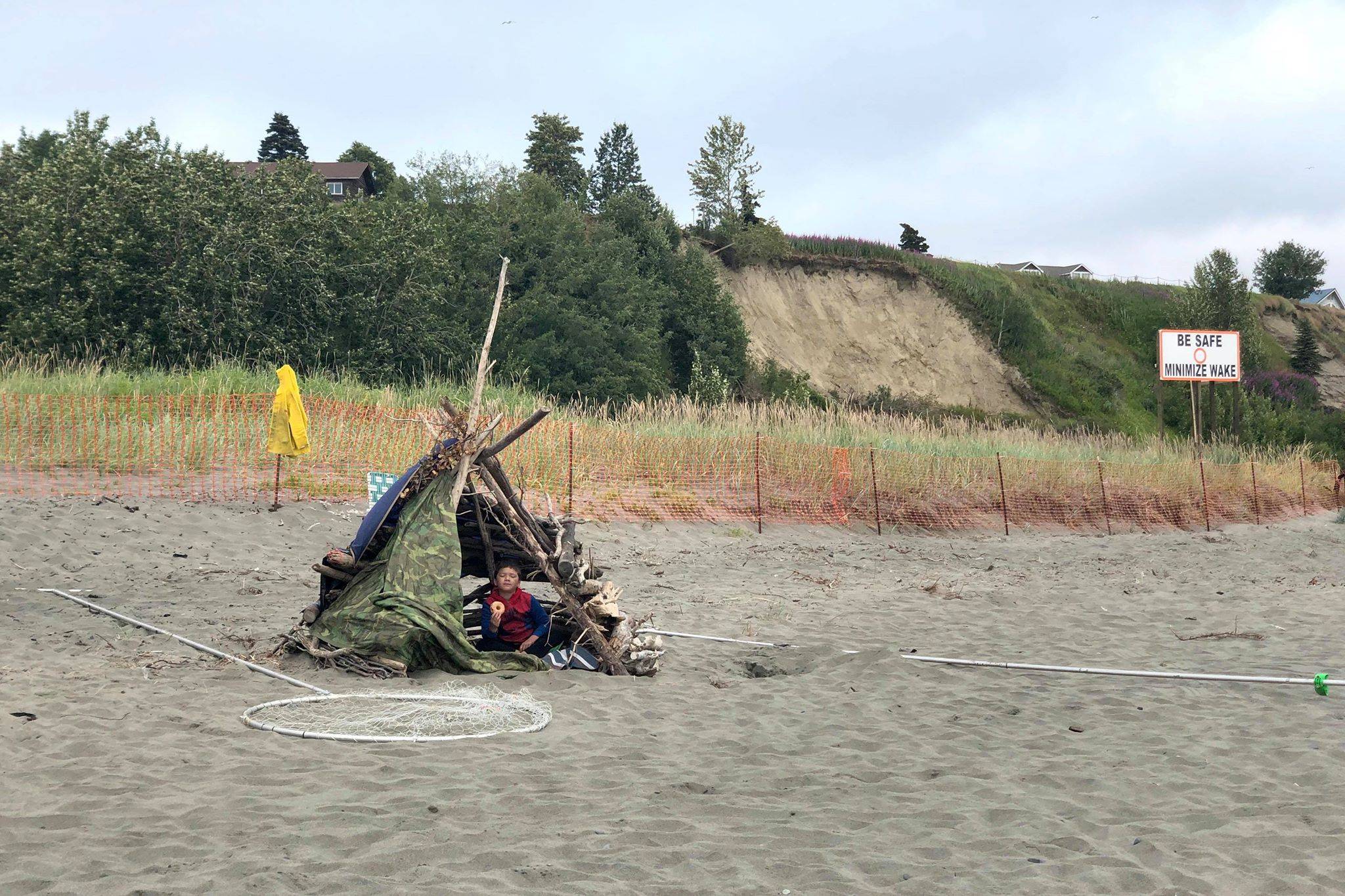 A child sits on the beach in a homemade shelter on the first day of the Kenai River personal use dipnet fishery, Wednesday, July 10, 2019, in Kenai, Alaska. (Photo by Victoria Petersen/Peninsula Clarion)