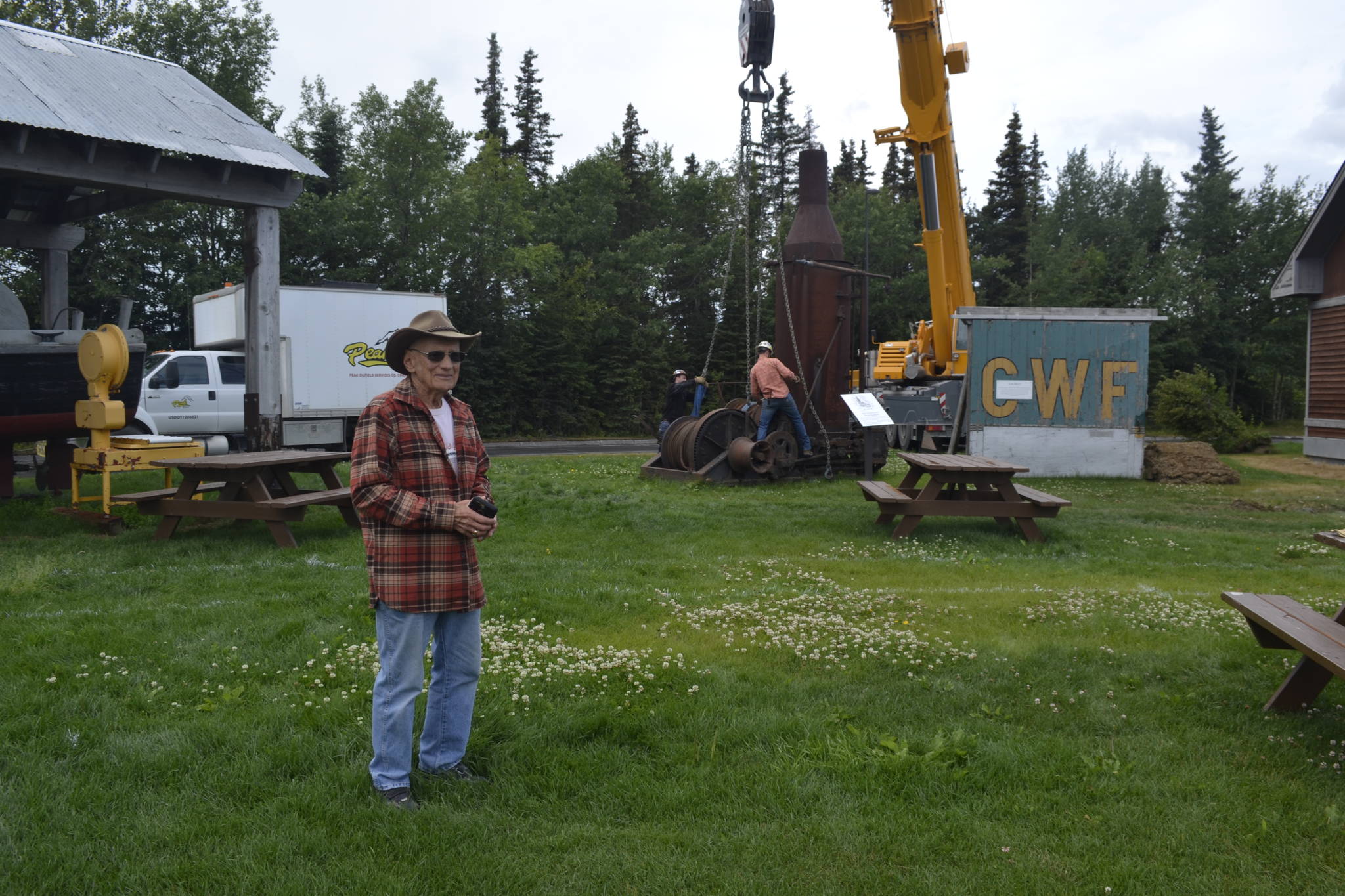 Dr. Peter Hansen stands in front of crane operators who are in the process of lifting an antique steam donkey engine at the Kenai Visitor and Cultural Center, where it will be relocated on the lawn to make room for a cabin that will act as a Kenai Bush doctors museum, Monday, July 15, 2019, in Kenai, Alaska. (Photo by Victoria Petersen/Peninsula Clarion)