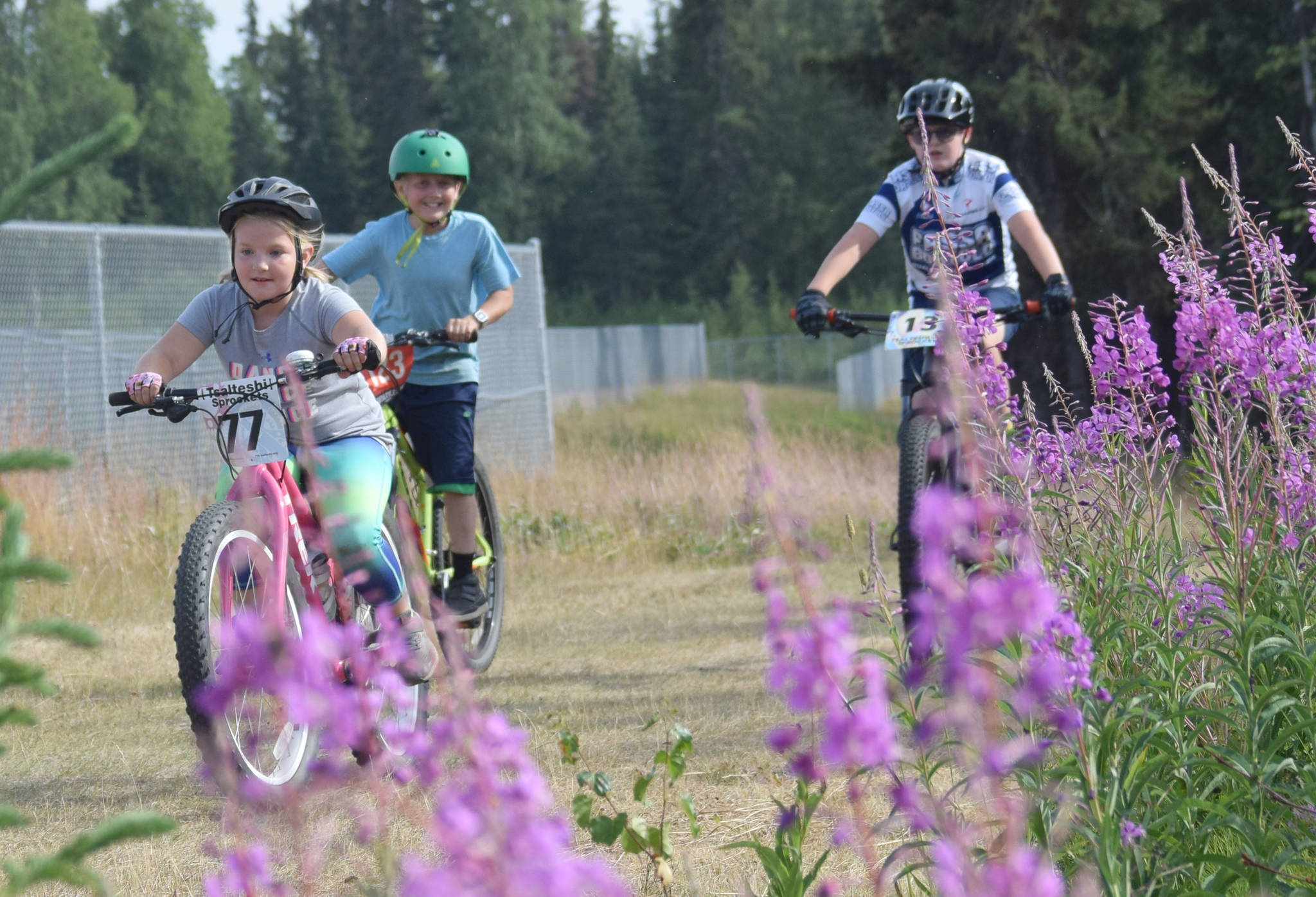 Addie Moore, 7, of Soldotna leads sweeper Will Smith, 12, of Kenai and Landen Showalter, 12, of Soldotna in the kids ramble at the Soldotna Cycle Series on Thursday, July 18, 2019, at Tsalteshi Trails. (Photo by Jeff Helminiak/Peninsula Clarion)