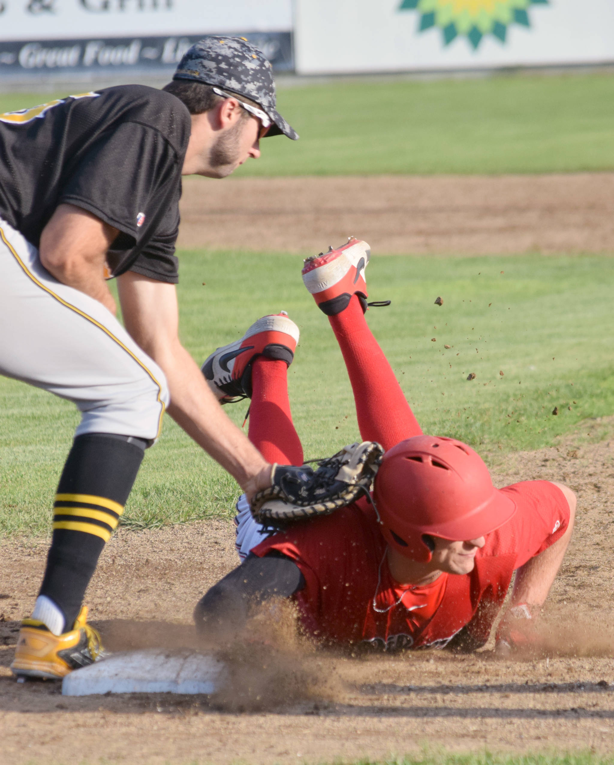 Peninsula Oilers’ Jaden Fein slides under the tag of Anchorage Bucs first baseman Ryan Sullivan on Thursday, July 25, 2019, at Coral Seymour Memorial Park in Kenai, Alaska. (Photo by Jeff Helminiak/Peninsula Clarion)