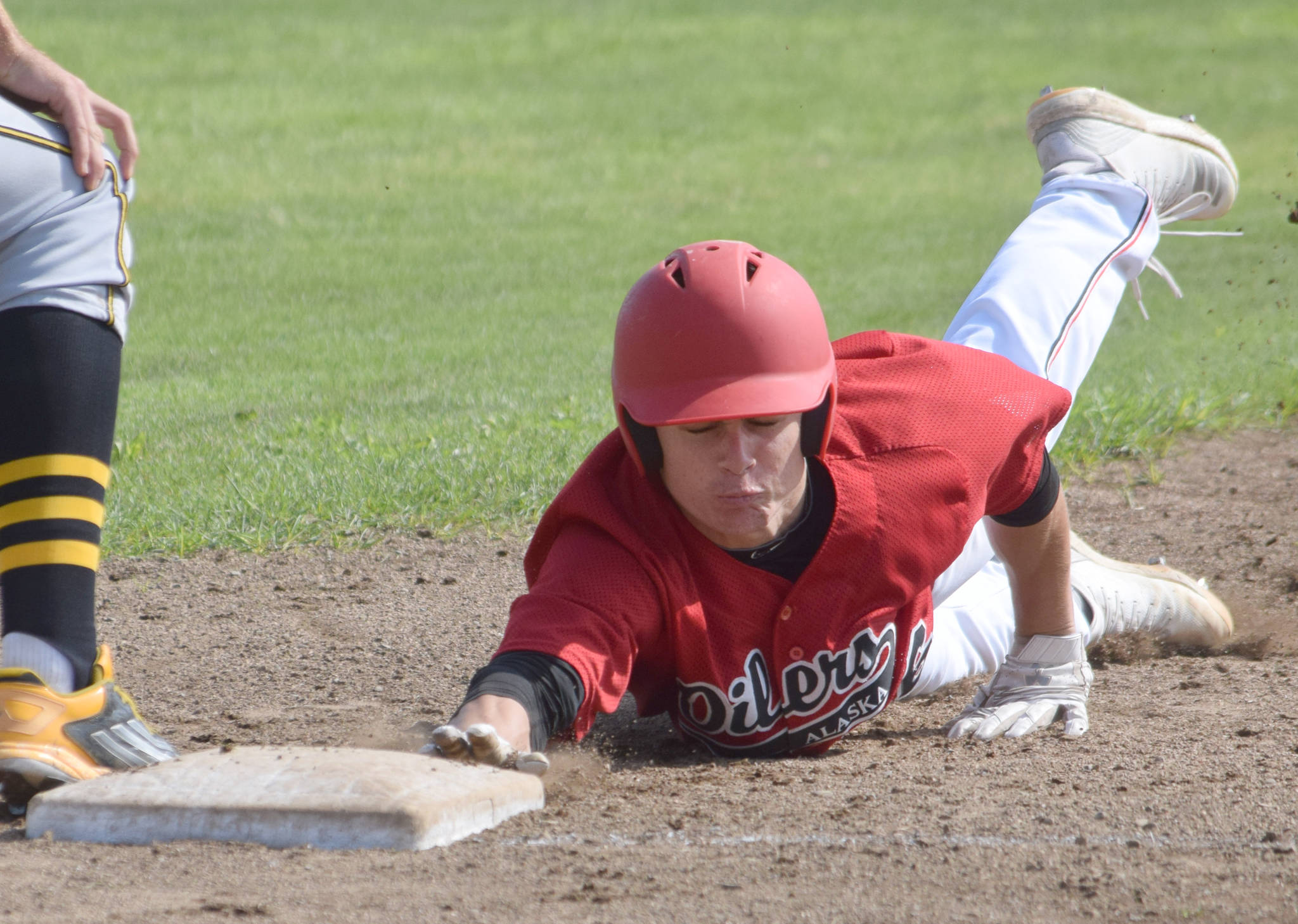 Peninsula Oilers’ Travis Bohall dives safely back into first base on Sunday, July 28, 2019, against the Anchorage Bucs at Coral Seymour Memorial Park in Kenai. (Photo by Jeff Helminiak/Peninsula Clarion)