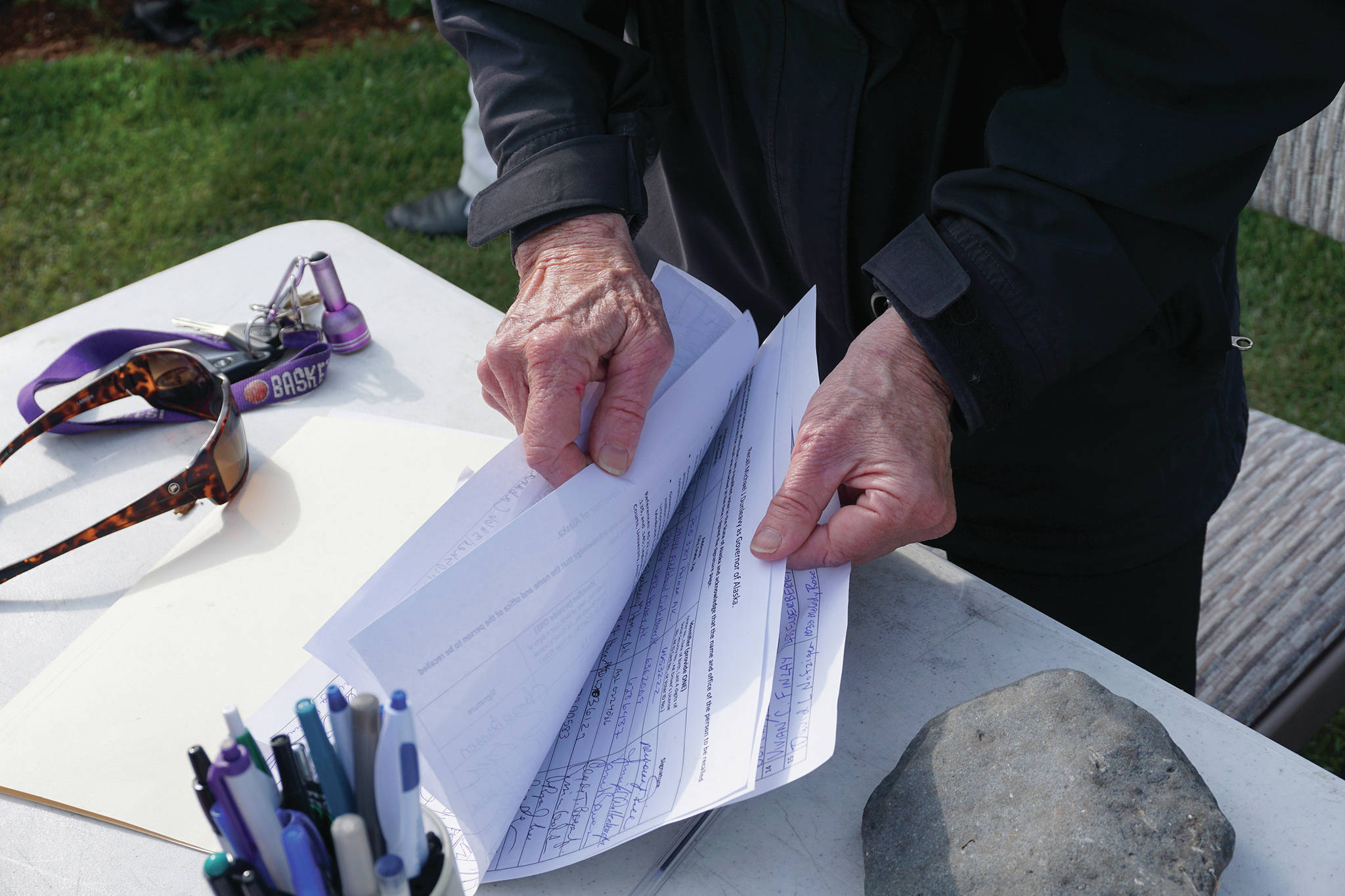Recall Dunleavy organizer Kathy Carssow flips through pages of signed forms to get a tally at a Recall Dunleavy rally held on Aug. 1, 2019, at WKFL Park in Homer, Alaska. (Photo by Michael Armstrong)