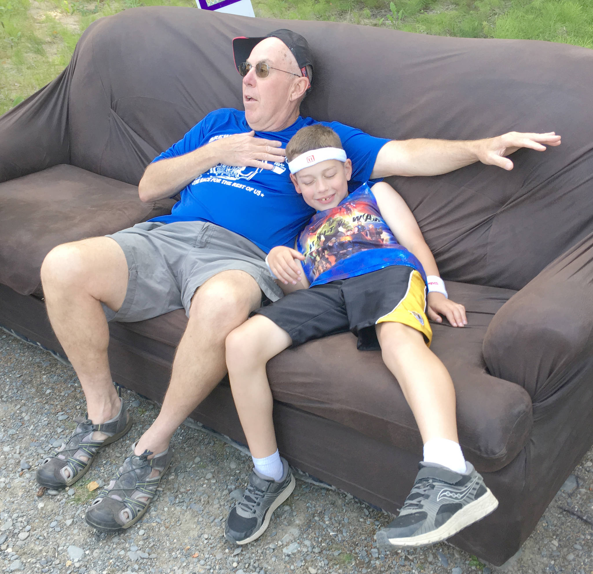 Nikiski’s Alan Bute and his grandson, Bennett Martin, donate $5 to take a break on the couch during the Brewery to Bathroom .5K “The race for the rest of us” on Sunday, Aug. 11, 2019, in Soldotna, Alaska. (Photo by Jeff Helminiak/Peninsula Clarion)