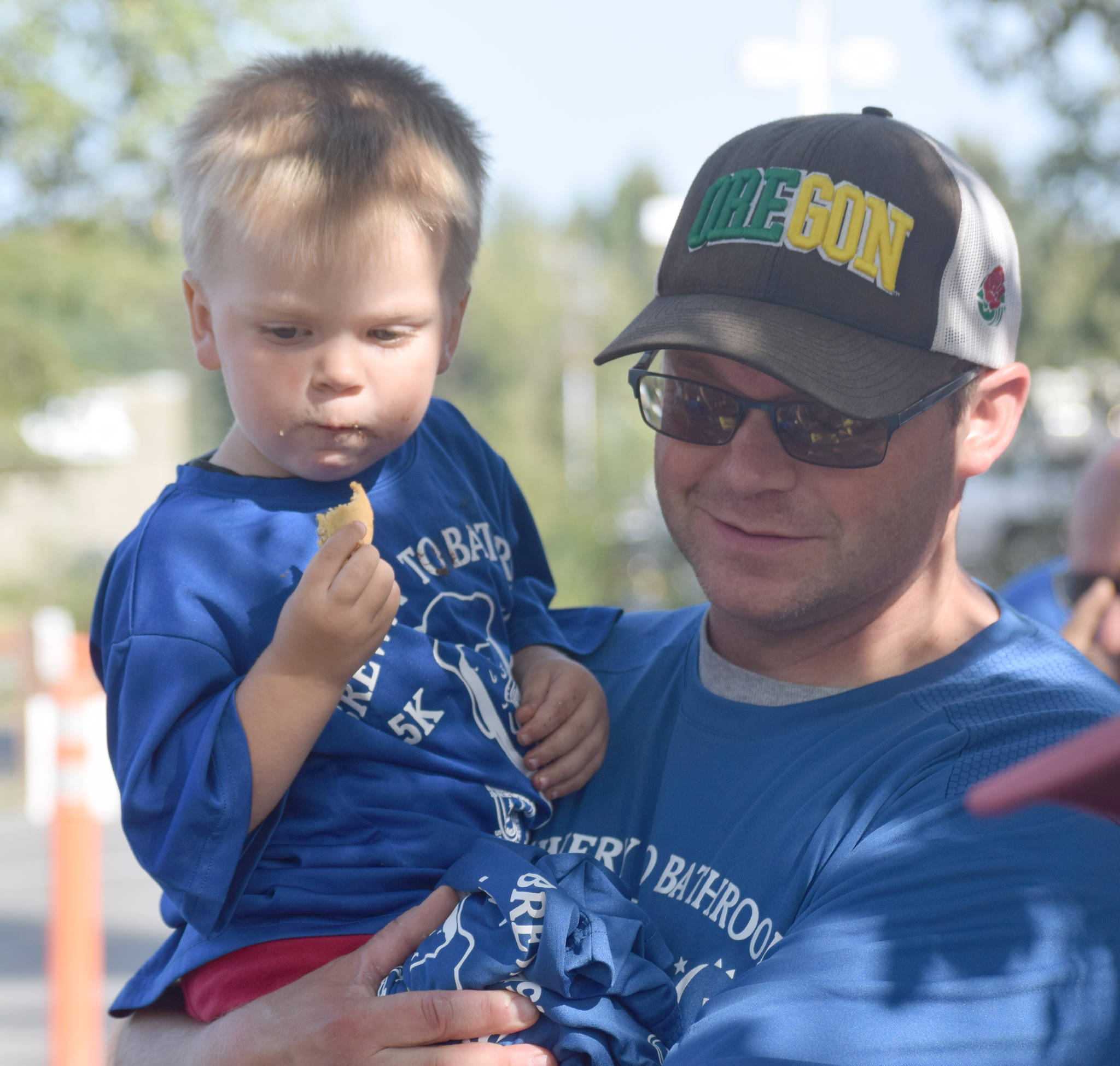 Mason Warfle, 2, is held by his father, Kenai’s Jason Warfle, at the Kenai Lions Club aid station at the halfway point of the Brewery to Bathroom .5K “The race for the rest of us” on Sunday, Aug. 11, 2019, in Soldotna, Alaska. (Photo by Jeff Helminiak/Peninsula Clarion)