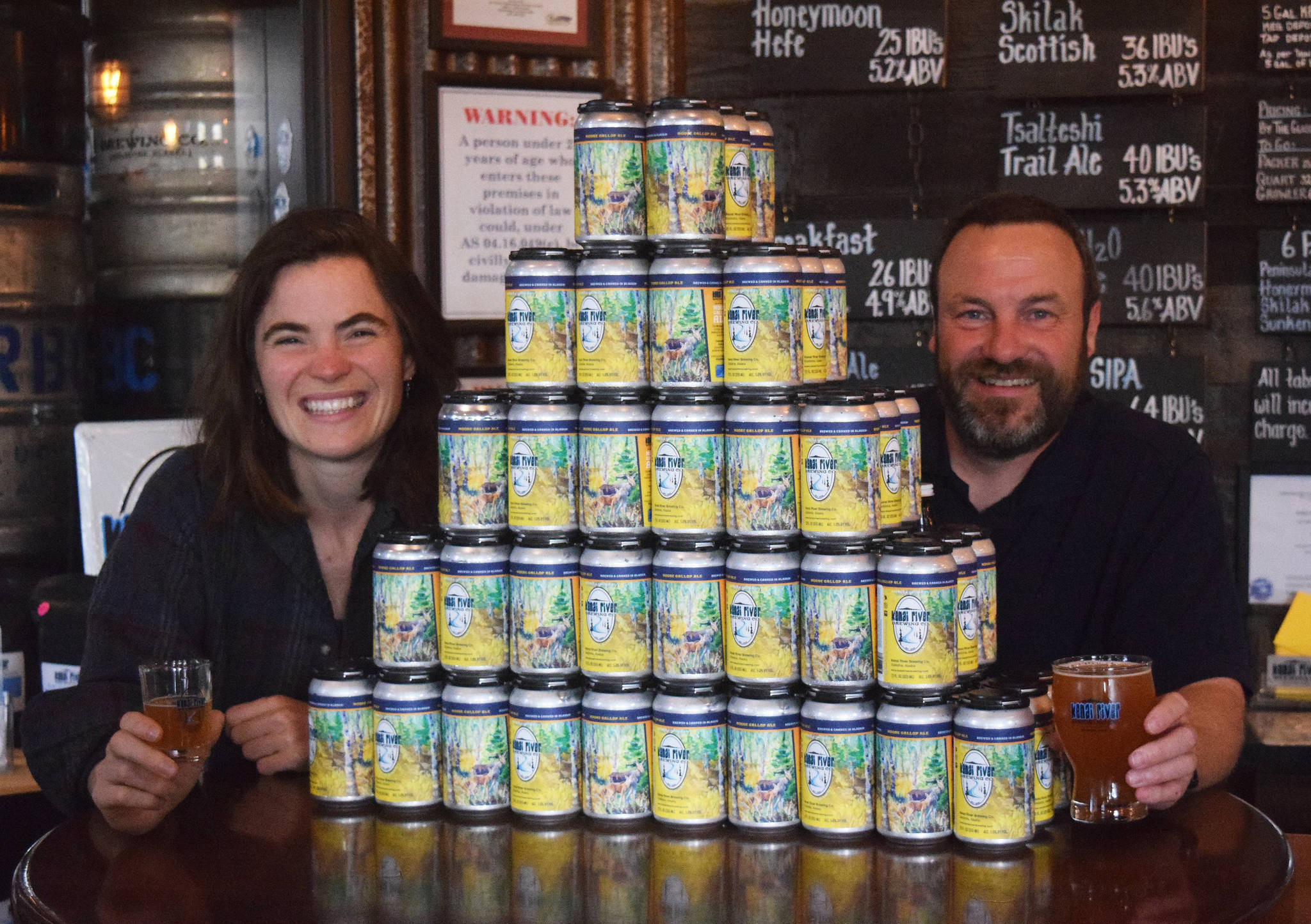 Photo by Joey Klecka/Peninsula Clarion                                 Soldotna artist Kaitlyn Vadla (left) and Kenai River Brewing owner Doug Hogue present the first batch of the brewery’s “Moose Gallop Ale” on Tuesday in Soldotna.