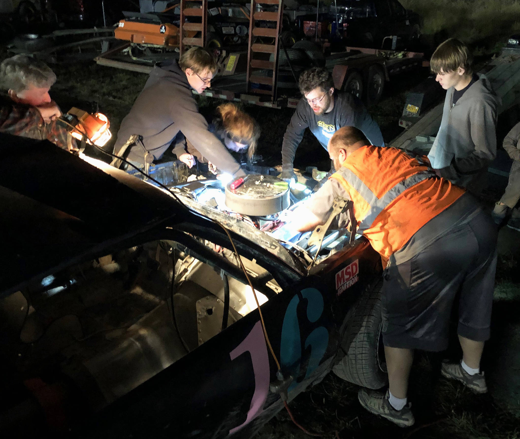 A crew of racers, mechanics and friends pore over the engine of Gracie Bass’ No. 16 A-Stock racer Friday, Sept. 6, 2019, at Twin City Raceway in Kenai, Alaska. (Photo by Joey Klecka/Peninsula Clarion)
