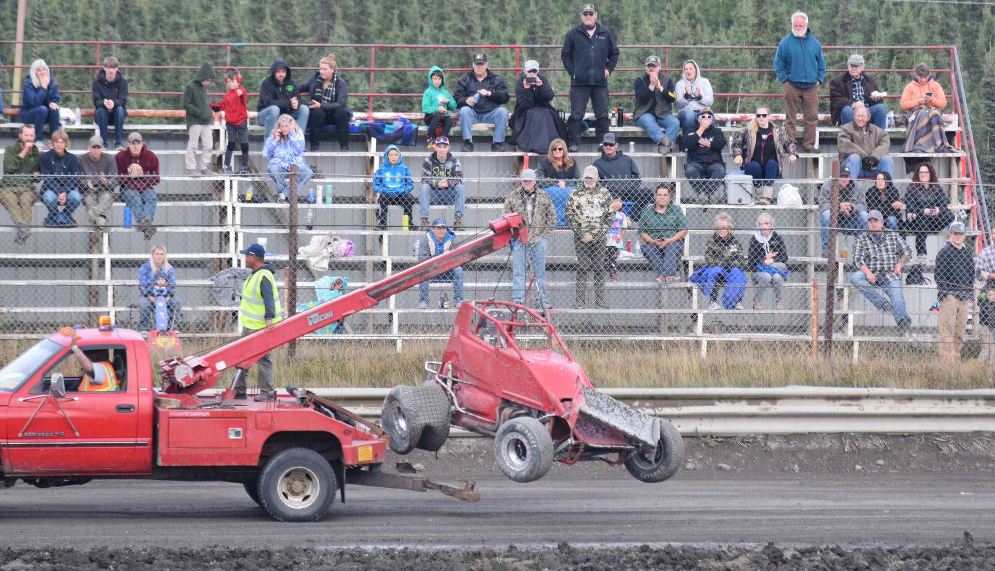 The crowd of race fans watch a tow truck pull the wrecked Sprint Car of John Mellish away Friday, Sept. 6, 2019, at Twin City Raceway in Kenai, Alaska. Mellish was unhurt in the incident. (Photo by Joey Klecka/Peninsula Clarion)