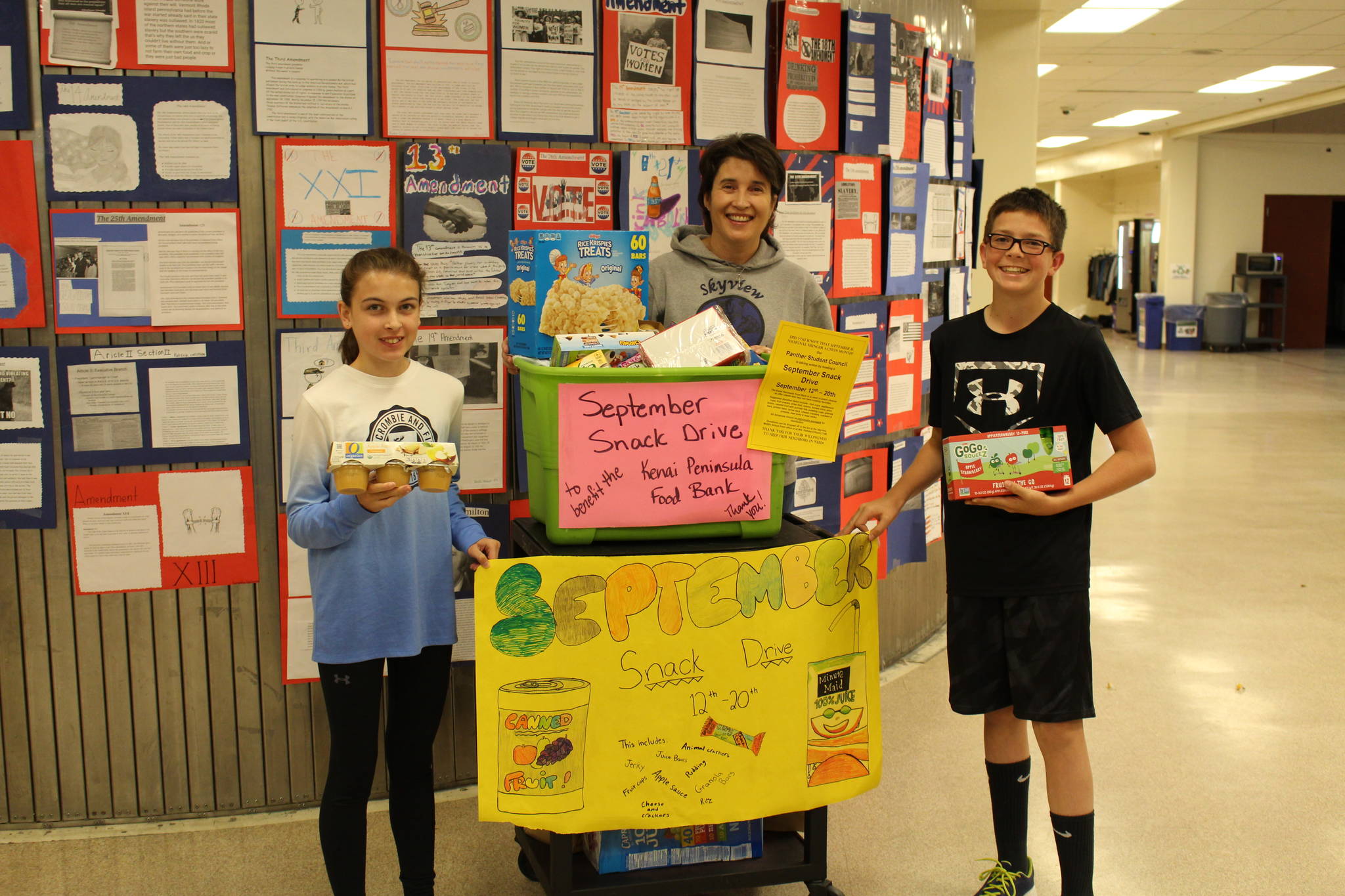 From left, eighth grader Avery Ciufo, student council adviser Sheilah Margaret Pothast and eighth grader Derrick Jones show off the food they’ve collected during their snack drive at Skyview Middle School in Soldotna, Alaska on Sept. 20, 2019. (Photo by Brian Mazurek/Peninsula Clarion)