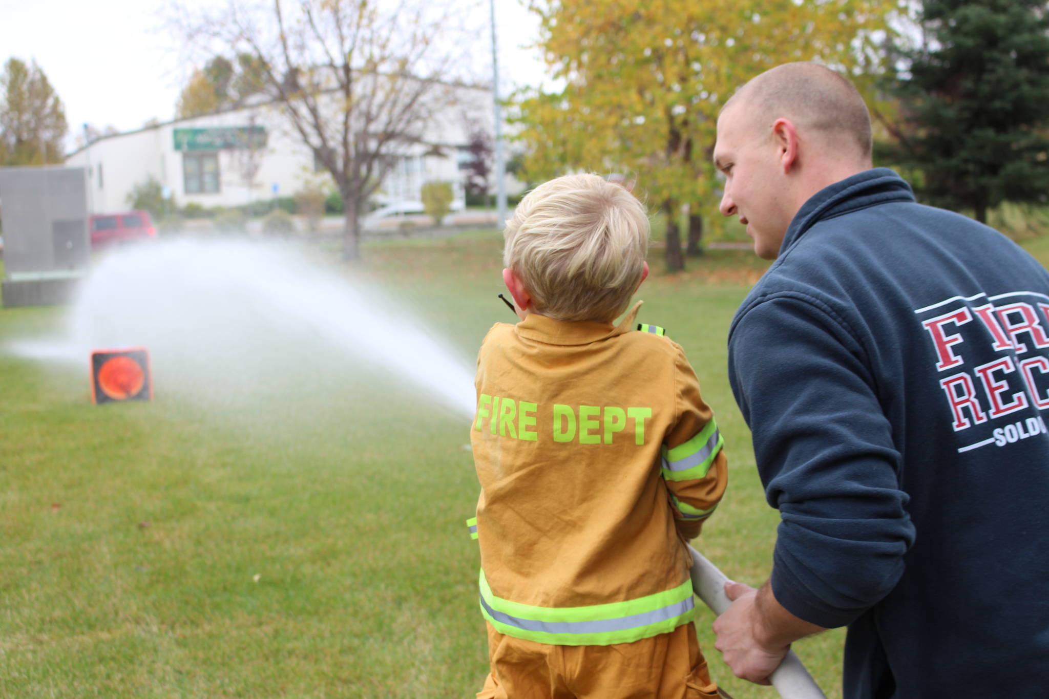 A young firefighter-in-training practices knocking down a water jug with a fire hose during the Central Emergency Services Open House at Fire Station 1 in Soldotna, Alaska on Sept. 28, 2019. (Photo by Brian Mazurek/Peninsula Clarion)