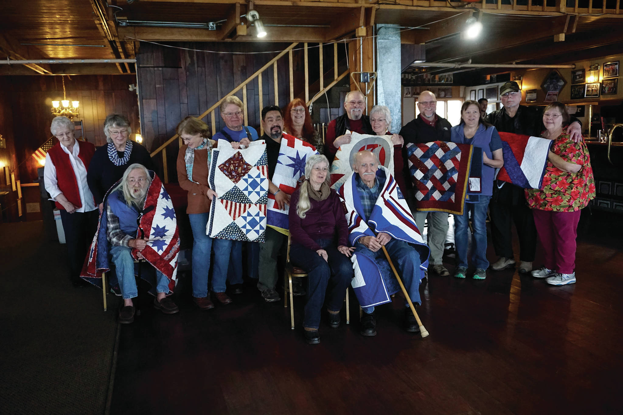 Veterans who received Quilts of Valor pose for a photograph at the Veterans Day lunch held at the Elks Lodge on Nov. 11, 2019, in Homer, Alaska. The quilts were made by the Kachemak Bay Quilters and presented as part of the national Quilts of Valor project. Since being founded by Catherine Roberts in 2003 while her son was deployed in Iraq, the program has given more than 235,000 quilts to military veterans, with almost 2,000 awarded in Alaska. Veterans who received quilts are, seated at left, John Benya; fifth from left, Troy Wise; sixth from left, Robert “R.J.” Carlough; eighth from left, Norman Mosher; ninth from left, in chair, Thomas Youngblood; fourth from right, Robert Fimon; and second from right, Nicholas Varney. (Photo by Michael Armstrong/Homer News)
