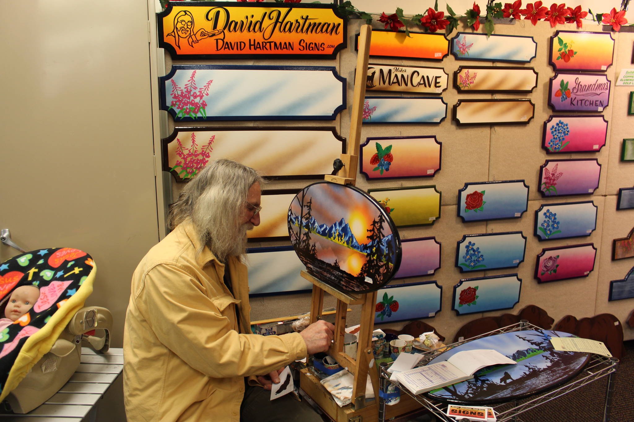 David Hartman paints and sells personalized signs at the annual Central Peninsula Hospital Auxiliary Holiday Bazaar in Soldotna, Alaska on Dec. 6, 2019. (Photo by Brian Mazurek/Peninsula Clarion)