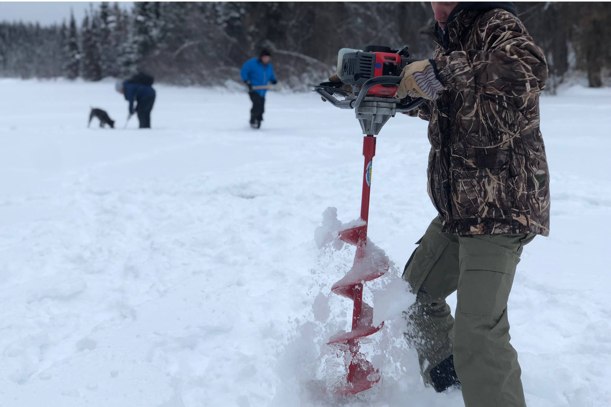 Dillon Jensen drills a hole into Paddle Lake off of Swan Lake Road in Sterling, Alaska on Feb. 2, 2020. (Photo by Victoria Petersen/Peninsula Clarion)