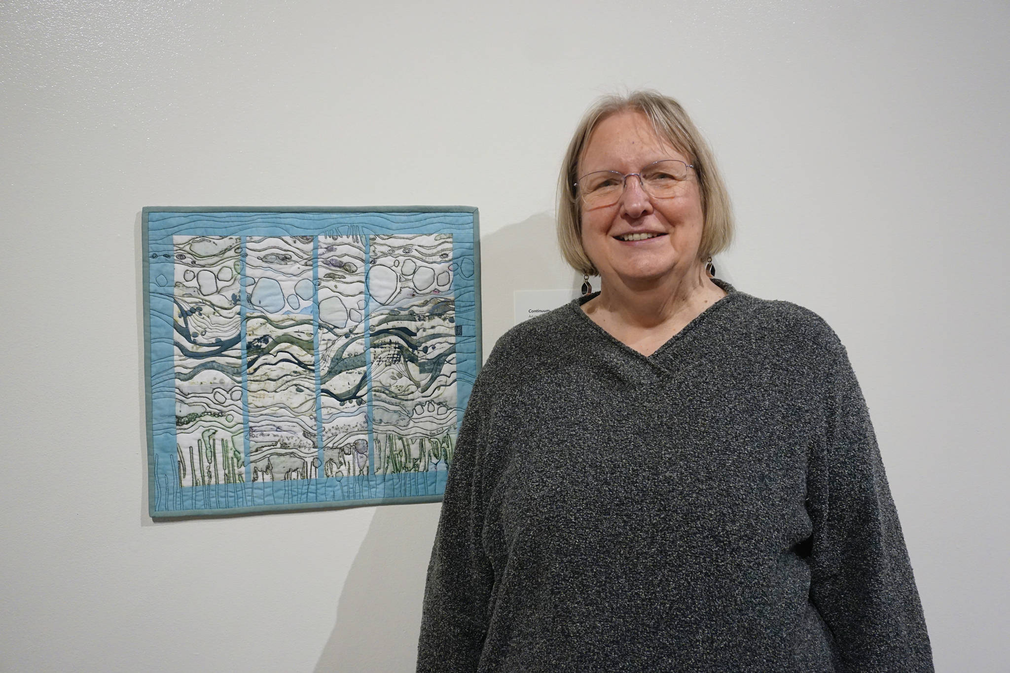 Ree Nancarrow stands next to her art quilt, “Continuum” on Feb. 4, 2020, at the Pratt Museum in Homer, Alaska. It was created in response to composer Libby Meyer’s “Turbulence.” Her work is part of “Denali Artists Respond to Music Inspired by Wilderness,” a collaboration between artists and composers showing Feb. 7-May 25, 2020, at the Pratt. (Photo by Michael Armstrong/Homer News)