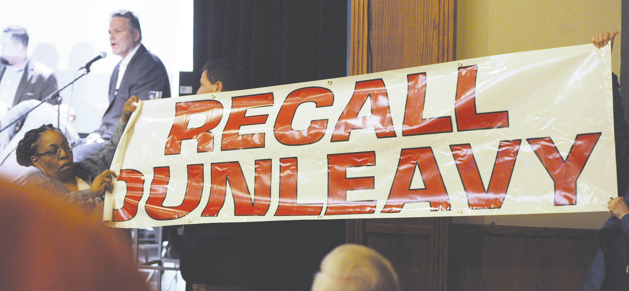 In this March 26, 2019, file photo, protesters unfurl a banner as Alaska Gov. Mike Dunleavy speaks during a roadshow with Americans for Prosperity in 49th State Brewing Company in Anchorage. The group opposing an effort to recall Alaska Gov. Mike Dunleavy plans to drop its court fight and instead gear up for a possible recall election. Stand Tall With Mike said Tuesday, Feb. 18, 2020, that it told its attorneys to withdraw its appeal before the Alaska Supreme Court. The group says recent court actions indicate that continuing to pursue the case in court would not be a productive use of resources. (Bill Roth/Anchorage Daily News via AP, File)