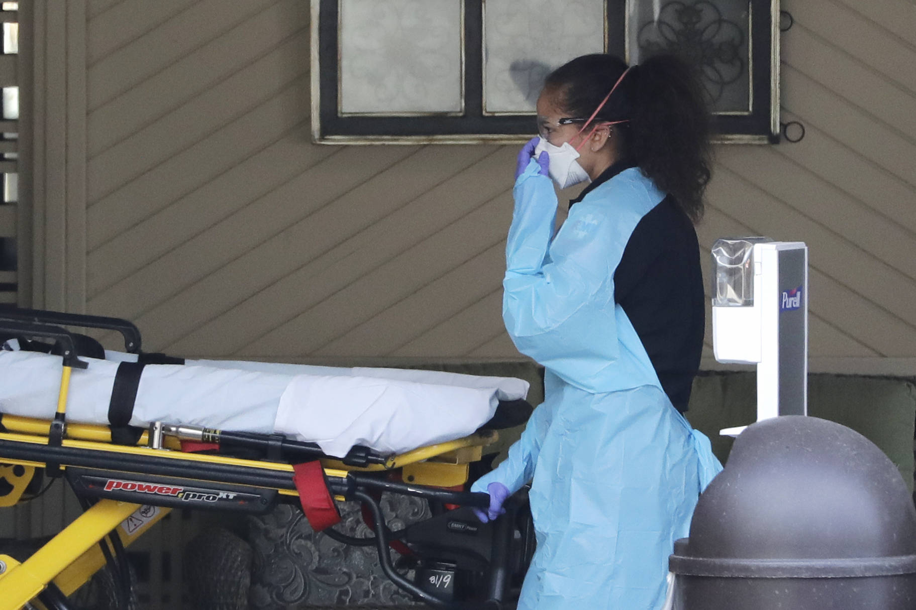 An ambulance worker adjusts her protective mask as she wheels a stretcher into a nursing facility where more than 50 people are sick and being tested for the COVID-19 virus, Saturday, Feb. 29, 2020, in Kirkland, Wash. (AP Photo/Elaine Thompson)