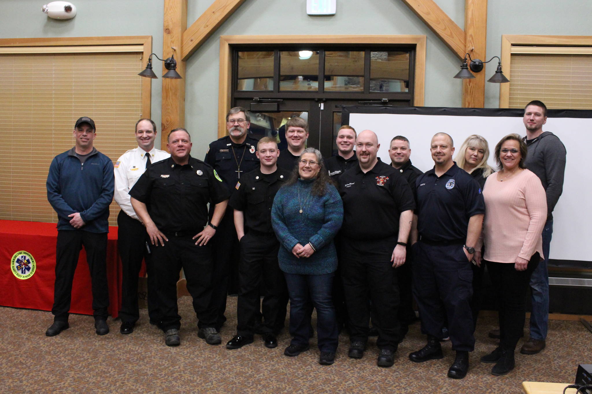 Amy Fisher, center, and the individuals who played a part in saving her life on Oct. 1, 2019 smile for a group photo at the Nikiski Fire Department’s 2019 Award Ceremony in the Nikiski Senior Center on Feb. 28, 2020. From left: Dominic Kuntz, Brian Crisp, JT Harris, Tim Tolar, TJ Cox, Vladislav Glushkov, Amy Fisher, Brandon Edwards, William Manuel, Stephen Robertson, Tony Smith, Laura Osborn, Carol Asp and Tony Besse. (Photo by Brian Mazurek/Peninsula Clarion)