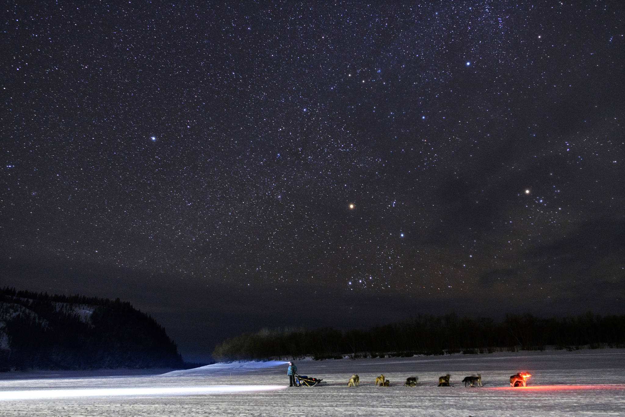 FILE - In this March 9, 2019 file photo Kristy Berington waits on the Innoko River for her sister, Anna Berington, after they both left Shageluk, Alaska, during the Iditarod Trail Sled Dog Race. Nearly 1,000 miles (1,600 kilometers) of unforgiving terrain, doused in deep snow this year, await them as they cross two mountain ranges, travel on the frozen Yukon River and navigate the treacherous and wind-whipped Bering Sea coast to old Gold Rush town of Nome. The winner is expected there about 10 or 11 days after the start. (Marc Lester/Anchorage Daily News via AP,File)