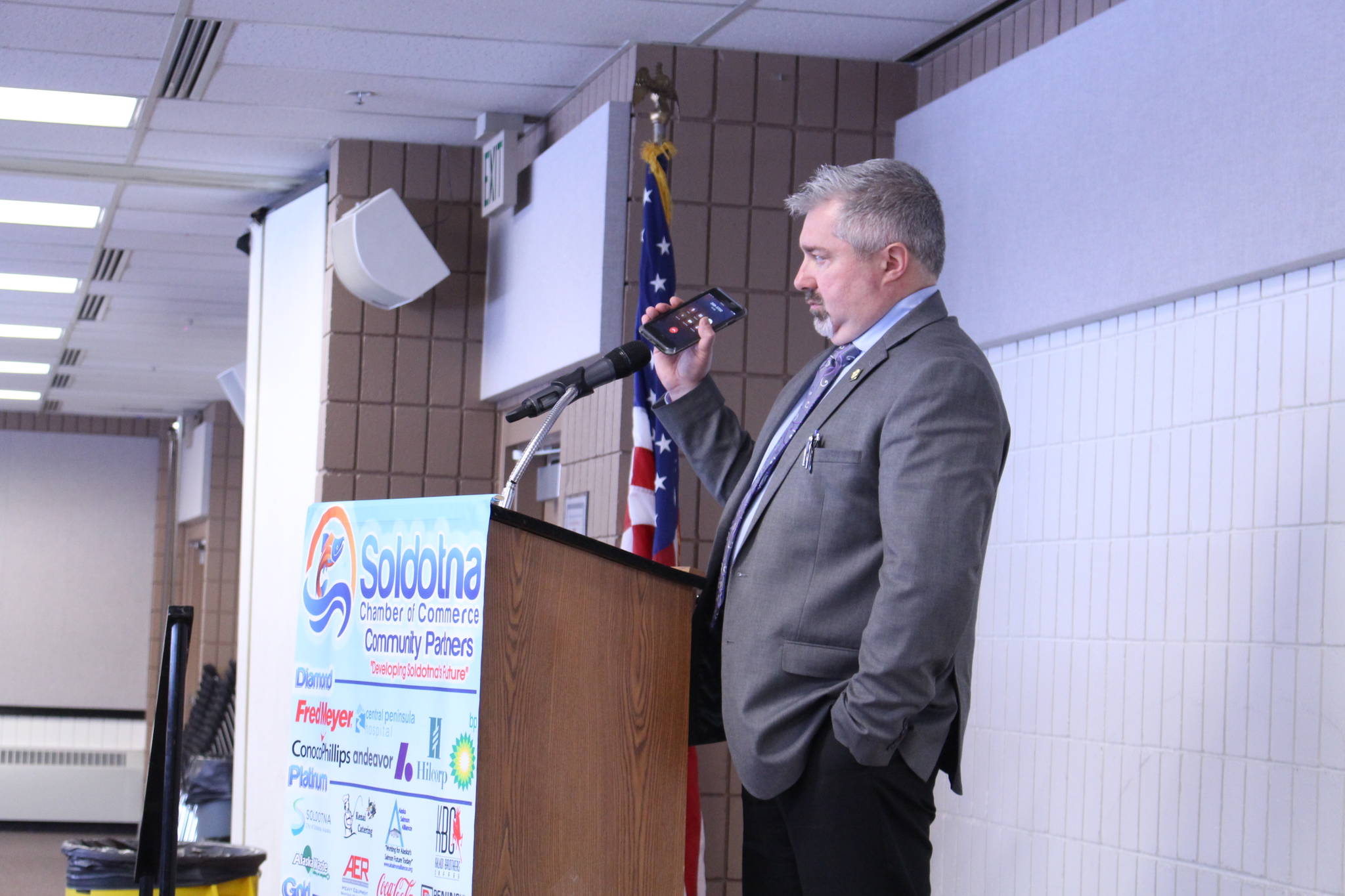 Dave Stieren, community outreach director for Gov. Mike Dunleavy, holds his phone up to the microphone as Dunleavy gives a remote speech to the Kenai and Soldotna Chambers of Commerce at the Soldotna Regional Sports Complex on Monday, March 9, 2020. (Photo by Brian Mazurek/Peninsula Clarion)