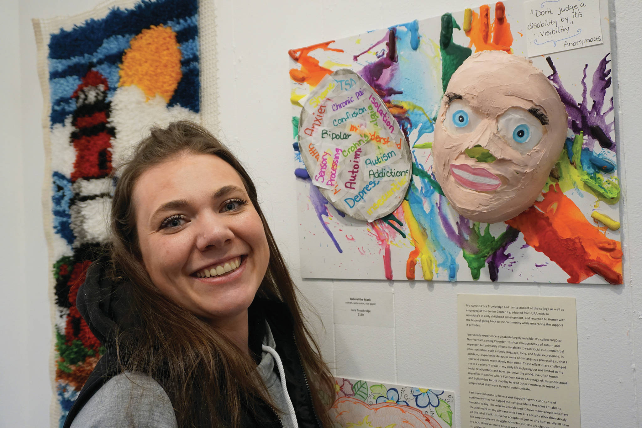 Cora Trowbridge stands by her art, “Behind the Mask,” on March 6, 2020, at the Disability Art Show at the Homer Council on the Arts in Homer, Alaska. (Photo by Michael Armstrong/Homer News)