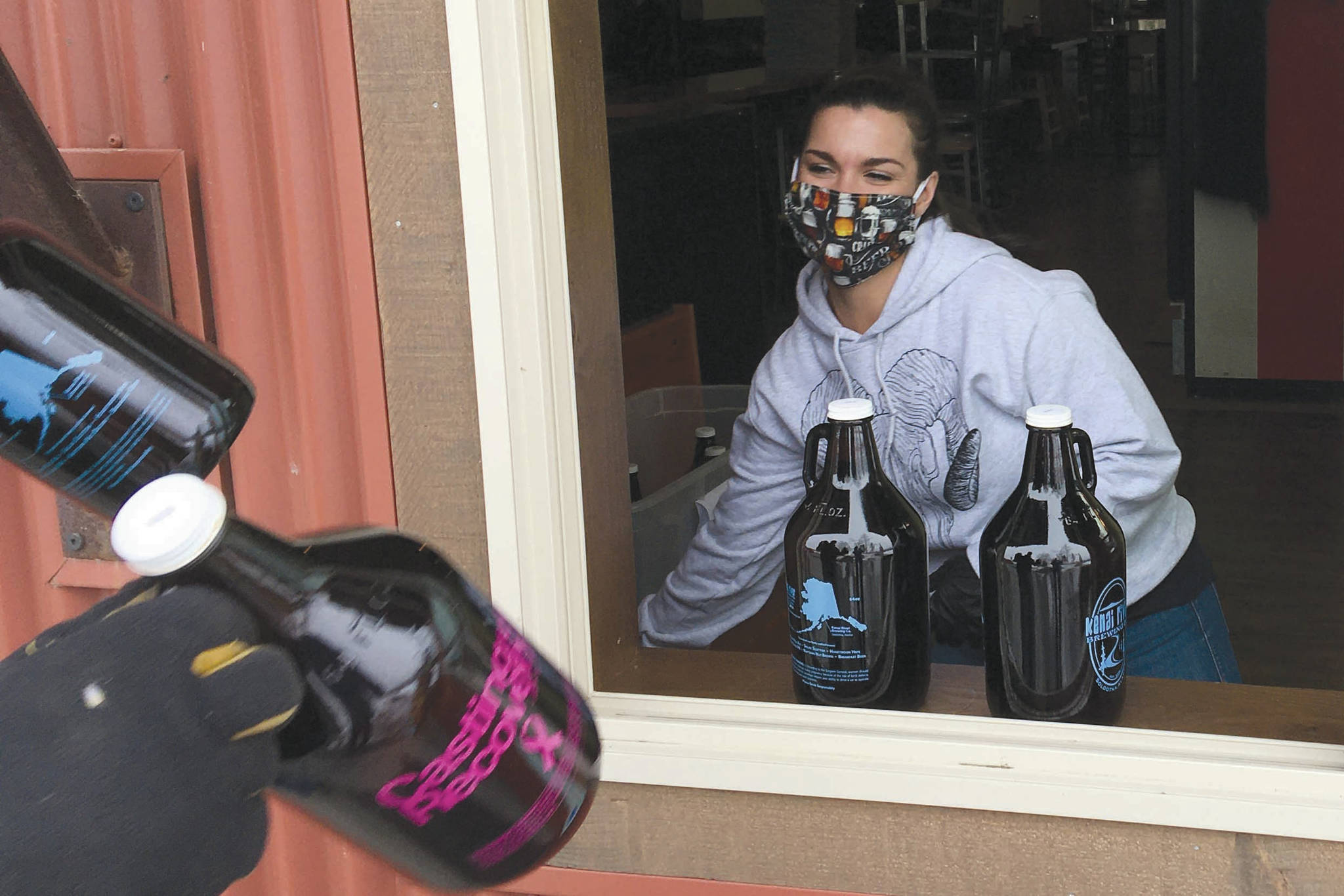 Server Taleasha Shane of Soldotna swaps out growlers with a customer Tuesday, April 7, 2020, at Kenai River Brewing in Soldotna, Alaska. Shane has worked for the brewery for about four years and said business has been picking up in the last week. “The community is awesome. They’ve been tipping well. They know the servers are losing customers and money. It’s hard.” (Photo by Jeff Helminiak/Peninsula Clarion)