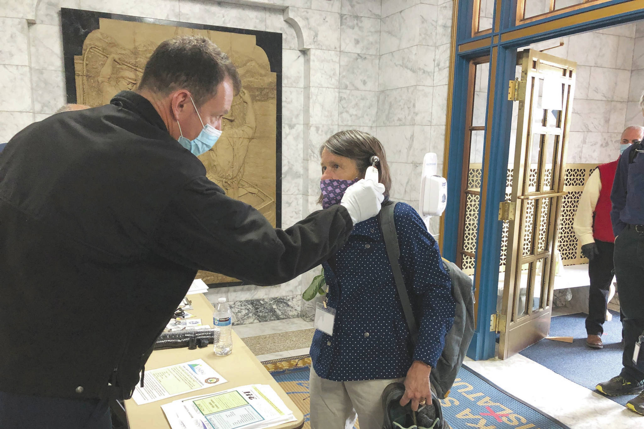 Alaska state Rep. Jennifer Johnston, an Anchorage Republican, gets her temperature taken by Roy Johnston, a captain with Capital City Fire/Rescue, at the state Capitol on Monday, May 18, 2020, in Juneau, Alaska. The Alaska Legislature planned to reconvene Monday to address use of federal coronavirus relief funds, with protocols in place aimed at guarding against the virus. (AP Photo/Becky Bohrer)