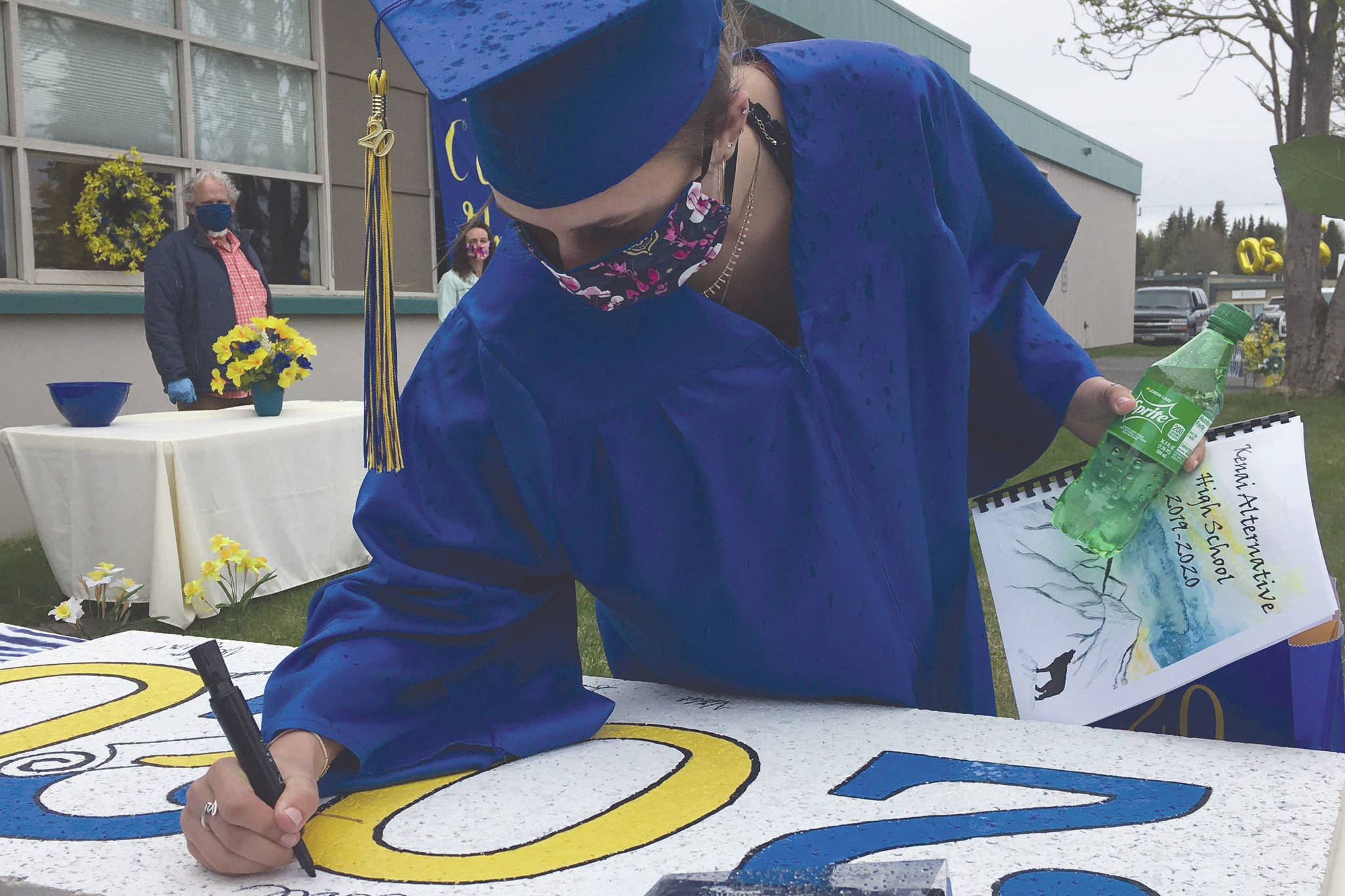Kenai Alternative High School graduate Elsie Daniels signs the ceiling tile for the Class of 2020 at the KAHS graduation Monday in Kenai, Alaska. The tile will join other graduating classes in the ceiling of the school office. (Photo by Jeff Helminiak/Peninsula Clarion)