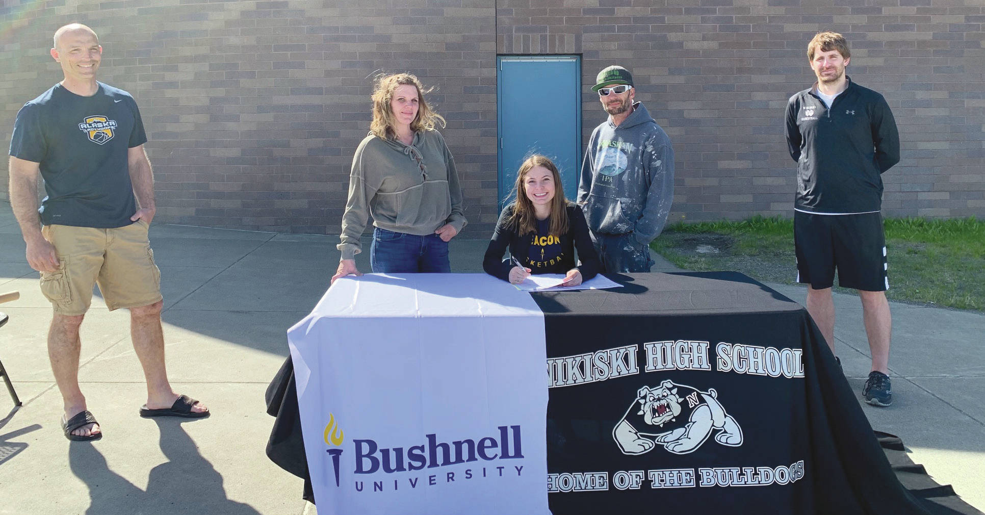 2020 Nikiski High School graduate America Jeffreys signs to play at Bushnell University in Eugene, Oregon, as Principal Dan Carstens, mother Kelly Jeffreys, father BJ Jeffreys and girls head basketball coach Rustin Hitchcock look on Wednesday, June 3, 2020. (Photo by Jeff Helminiak/Peninsula Clarion)