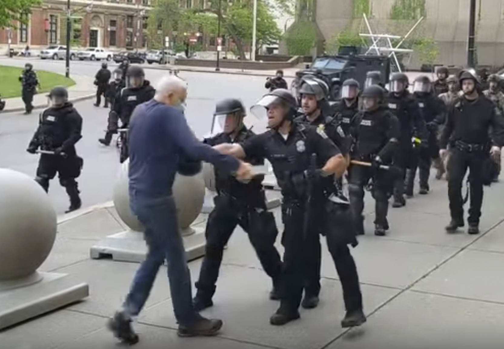 In this image from video provided by WBFO, a Buffalo police officer appears to shove a man who walked up to police Thursday, June 4, 2020, in Buffalo, N.Y. Video from WBFO shows the man appearing to hit his head on the pavement, with blood leaking out as officers walk past to clear Niagara Square. Buffalo police initially said in a statement that a person was injured when he tripped & fell, WIVB-TV reported, but Capt. Jeff Rinaldo later told the TV station that an internal affairs investigation was opened. Police Commissioner Byron Lockwood suspended two officers late Thursday, the mayors statement said. (Mike Desmond | WBFO via AP)