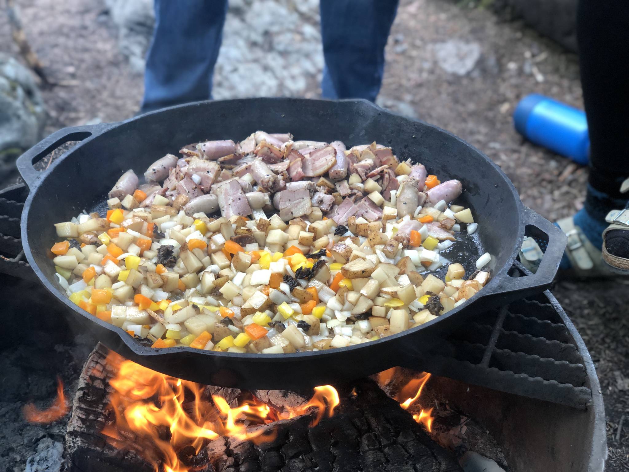 Hash with bacon, potatoes, cheese, sausage, chopped bell peppers and morel mushrooms are prepared on a fire pit, June 19, in the Copper River Valley. (Photo by Victoria Petersen/Peninsula Clarion)