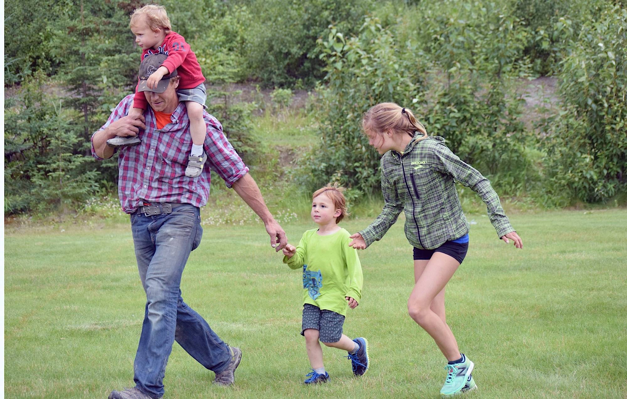 Chad Anderson of Kasilof and Allie Ostrander guide Everett Anderson, 3, to the finish line Wednesday, July 19, 2017, at the Salmon Run Series at Tsalteshi Trails. Getting the free ride on Chad’s shoulders is Ben Anderson, 2. (Photo by Jeff Helminiak/Peninsula Clarion)