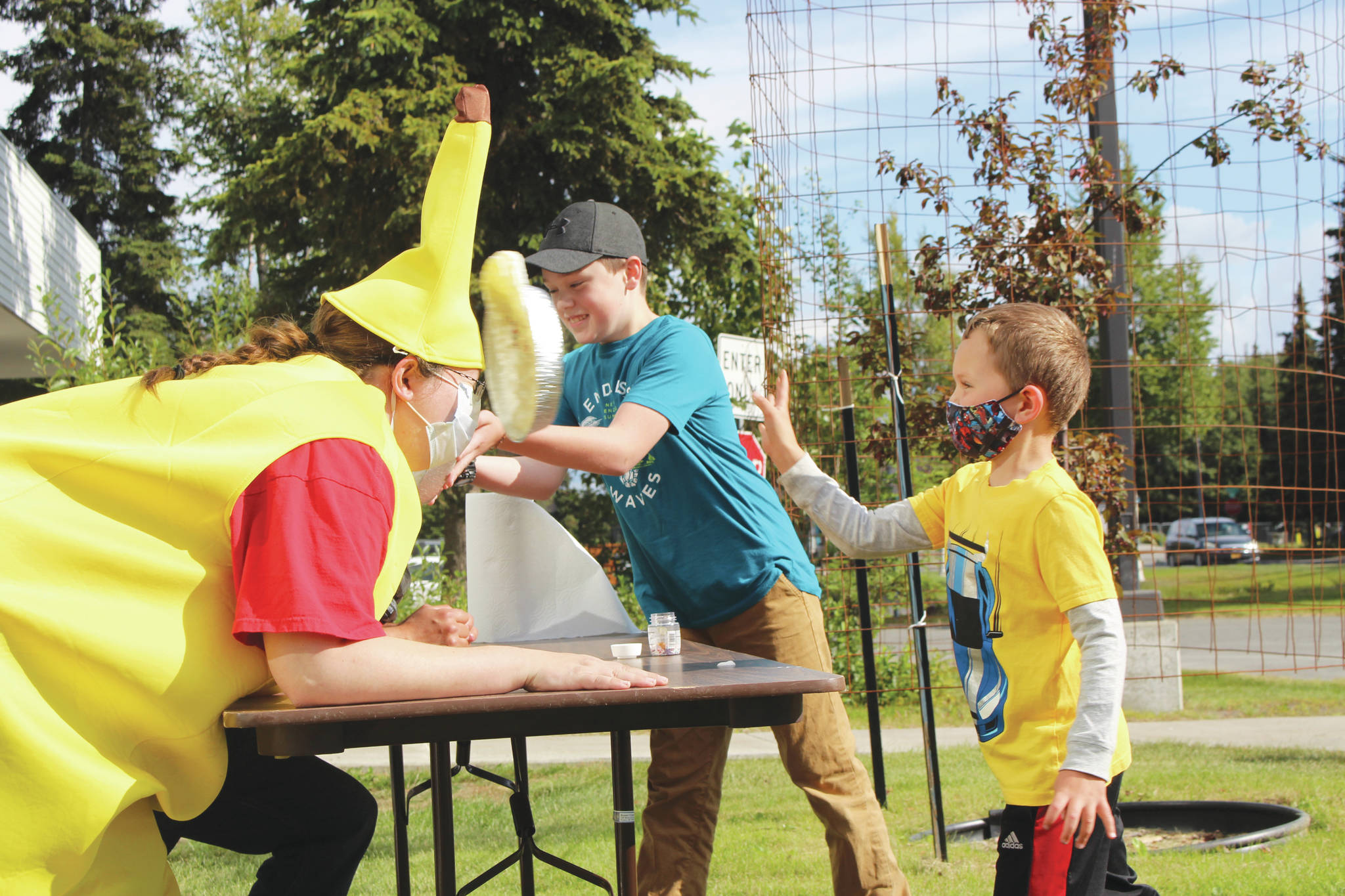 Brian Mazurek / Peninsula Clarion                                 Liam McCloud, right, and Josh Bolling, center, throw pies in the faces of Kenai Librarians Bethany McMilin, left, and James Adcox outside the Kenai Library on Wednesday. McCloud and Bolling won the right to throw the pies for participating in the library’s summer reading program, which went virtual this year.