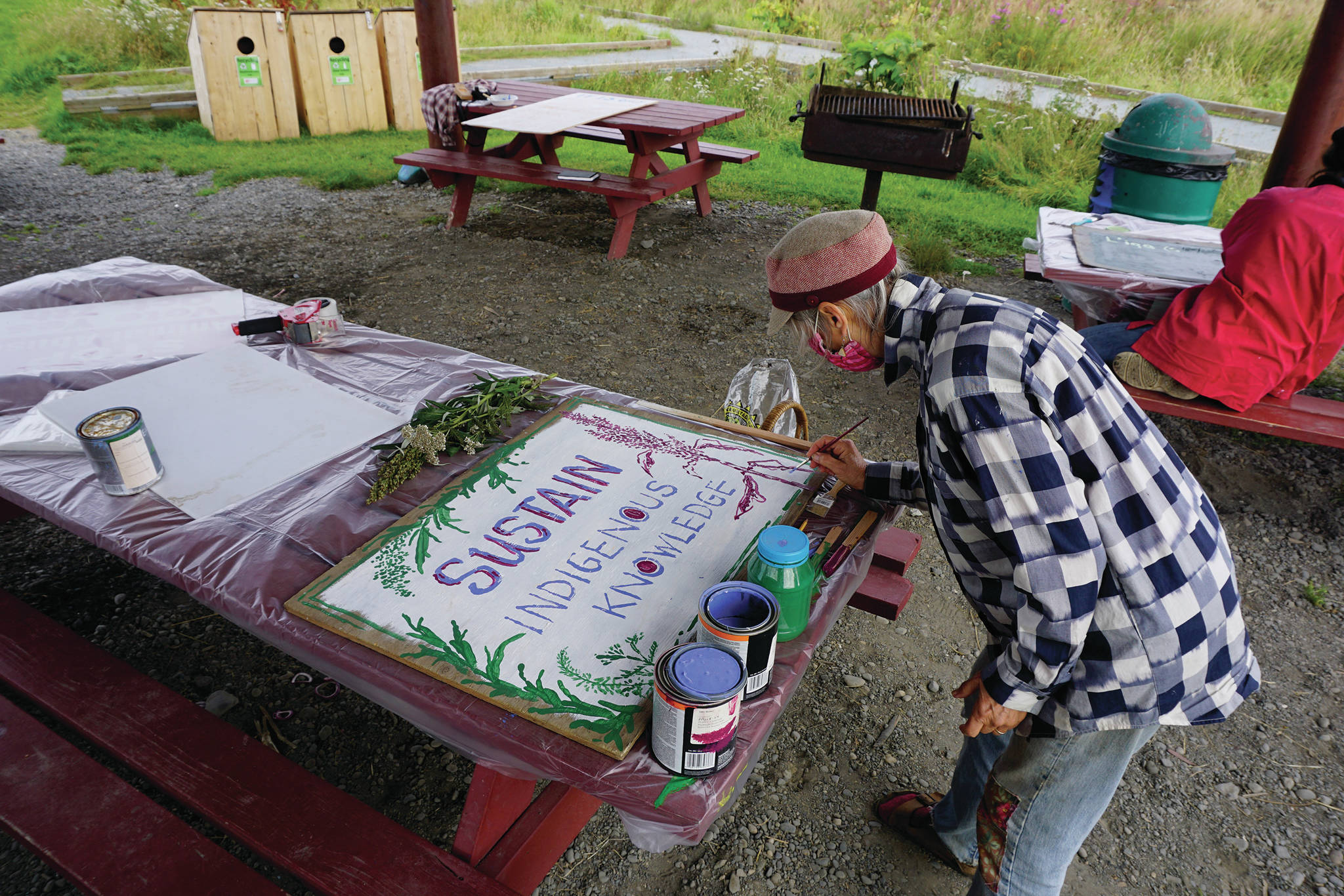 Debi Poore paints a sign at “Land Acknowledgement in Action: Sign Installation” last Saturday, Aug. 22, 2020, at the Bishop’s Beach pavillion — the area known by the Dena’ina people as “Tuggeht,” or “at the water’s edge.” (Photo by Michael Armstrong/Homer News.