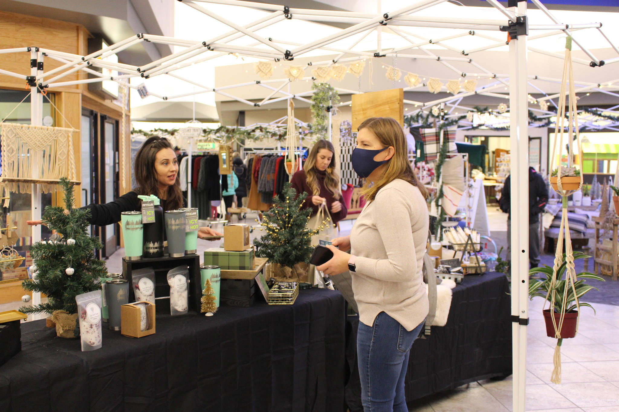 Dharmic Spruce owner Branden Elde, left, of Homer, shows off her wares to Amy Frapp, right, of Soldotna, during the Merry Little Christmas Market at the Peninsula Center Mall in Soldotna, Alaska, on Nov. 7, 2020. (Photo by Brian Mazurek/Peninsula Clarion)