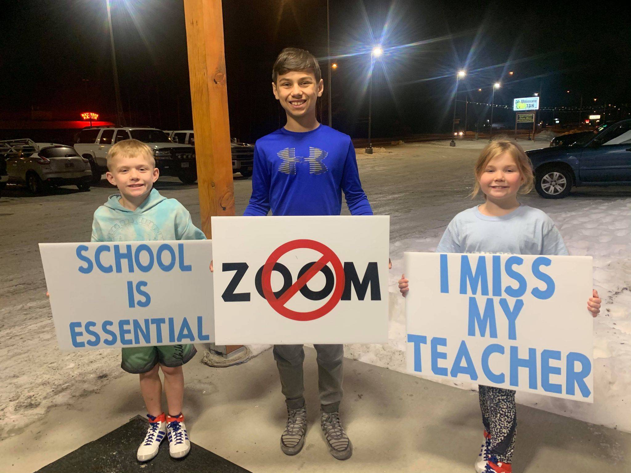 From left to right, Peyton Cobb, Mason Bock and Myla Cobb hold signs opposing remote learning on Monday, Dec. 14. (Photo courtesy of Andie Bock).