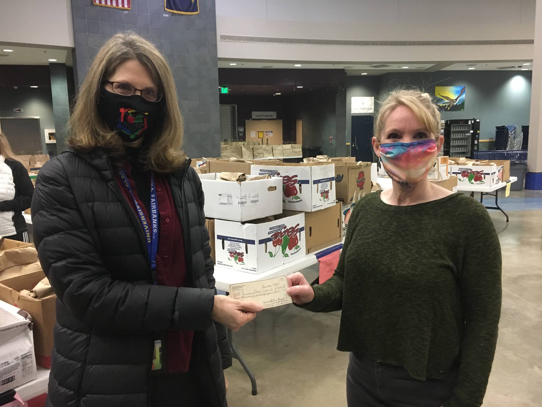 Catherine Pusich, left, hands a check from the Juneau Education Support Staff to Adrianne Schwartz to clear all money owed for school meals at Thunder Mountain High School on Dec. 21, 2020. (Michael S. Lockett / Juneau Empire)