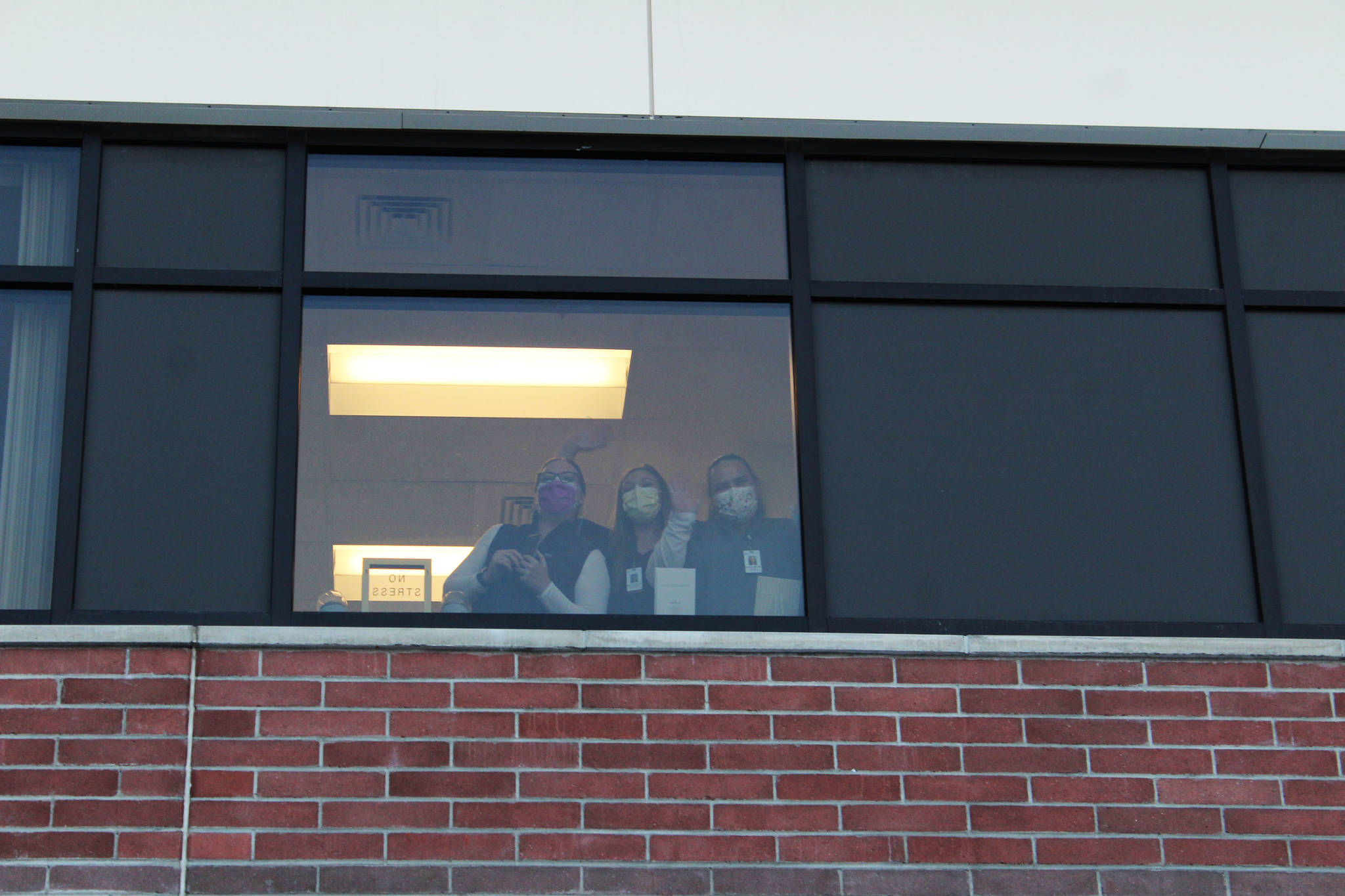 Ashlyn O’Hara/Peninsula Clarion
Health care workers wave from inside of Central Peninsula Hospital while awaiting the delivery of the facility’s first shipment of COVID-19 vaccines on Dec. 16 in Soldotna.