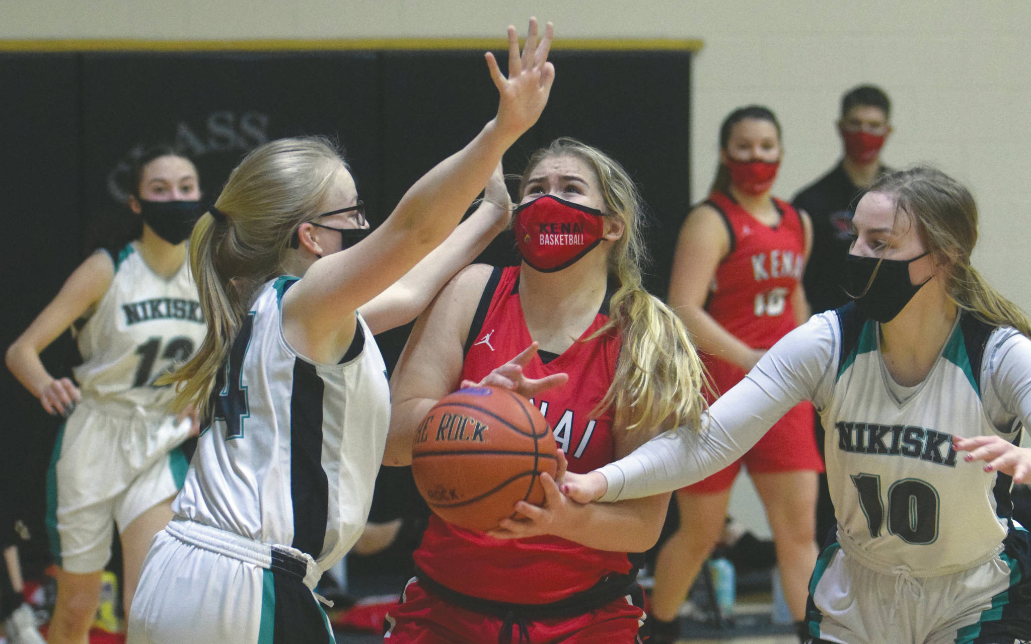 Kenai Central’s Emma Beck is fouled by Nikiski’s Lillian Carstens and guarded by Avery White on Thursday, Feb. 4, 2021, at Nikiski High School in Nikiski, Alaska. (Photo by Jeff Helminiak/Peninsula Clarion)