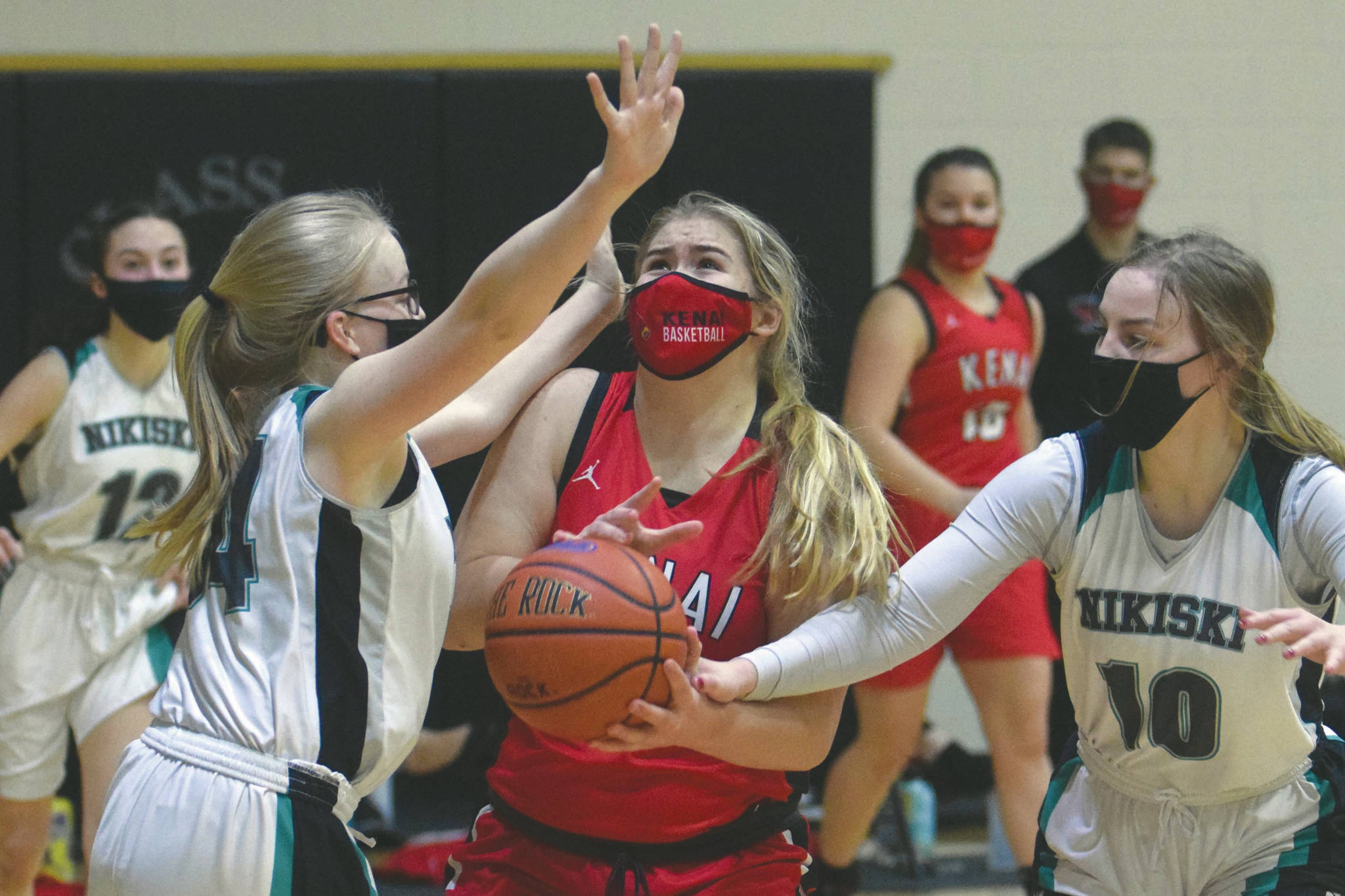 Kenai Central's Emma Beck is fouled by Nikiski's Lillian Carstens and guarded by Avery White on Thursday, Feb. 4, 2021, at Nikiski High School in Nikiski, Alaska. (Photo by Jeff Helminiak/Peninsula Clarion)