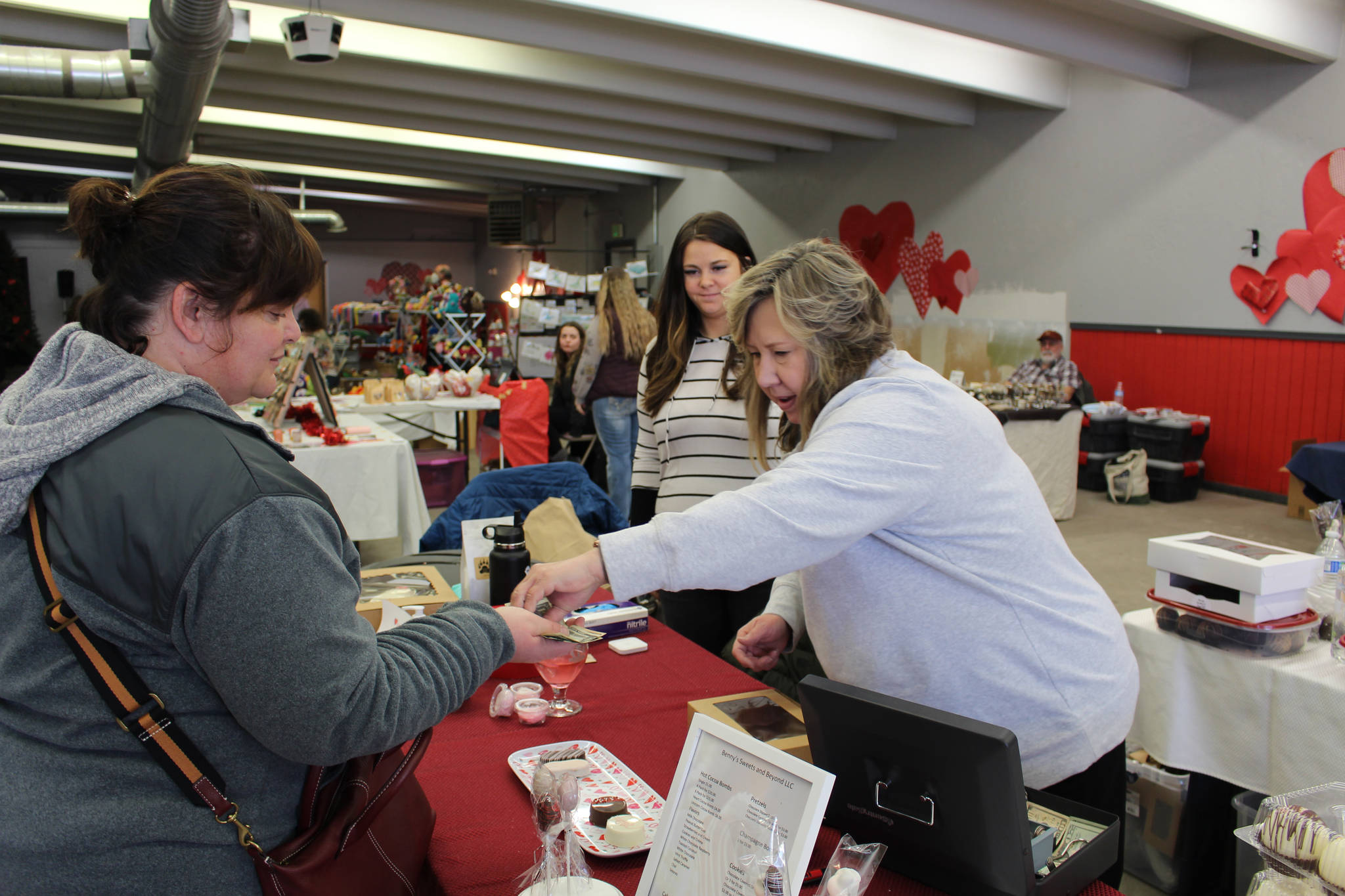 Robin Hahn, left, of Soldotna buys some hot cocoa bombs from Sherian Soares, right, and Ashley Soares, center, owners of Benny’s Sweets and Beyond, at a Valentine’s Bazaar in Soldotna, Alaska on Feb. 6, 2021. (Photo by Brian Mazurek/Peninsula Clarion)