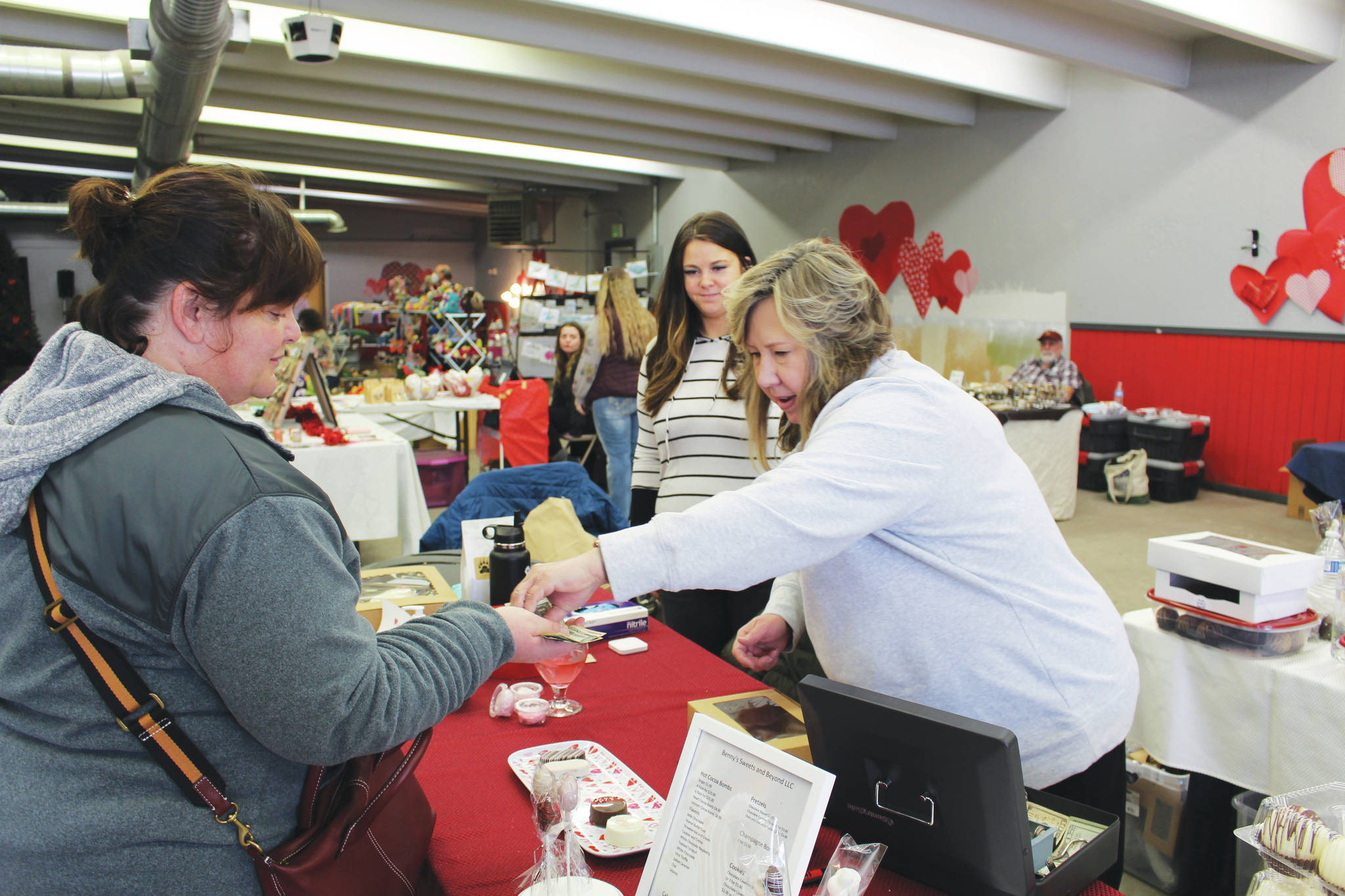 Photo by Brian Mazurek/Peninsula Clarion 
Robin Hahn, left, of Soldotna buys some hot cocoa bombs from Sherian Soares, right, and Ashley Soares, center, owners of Benny’s Sweets and Beyond, at a Valentine’s Bazaar in Soldotna on Saturday.