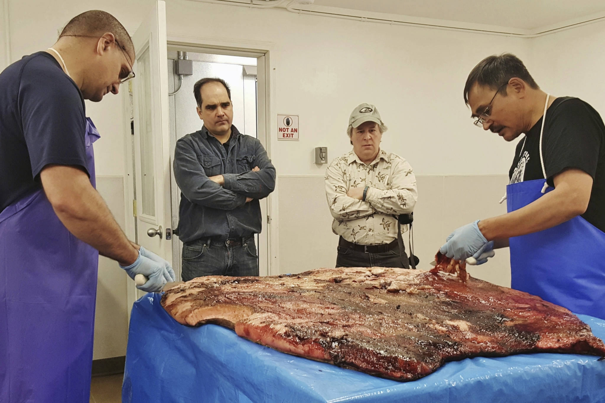 In this Oct. 28, 2016, photo provided by the Maniilaq Association, Alex Whiting, left, and Cyrus Harris, right, are observed by Chris Sannito, second from left, and Brian Himelbloom, third from left, of the Kodiak Seafood and Marine Science Center as they trim and clean seal blubber in Kotzebue, Alaska. In January 2021, the Alaska Department of Environmental Conservation approved seal oil to be served at a Maniilaq elder care home, believed to be a first for seal oil in the U.S.  (Maniilaq Association via AP)