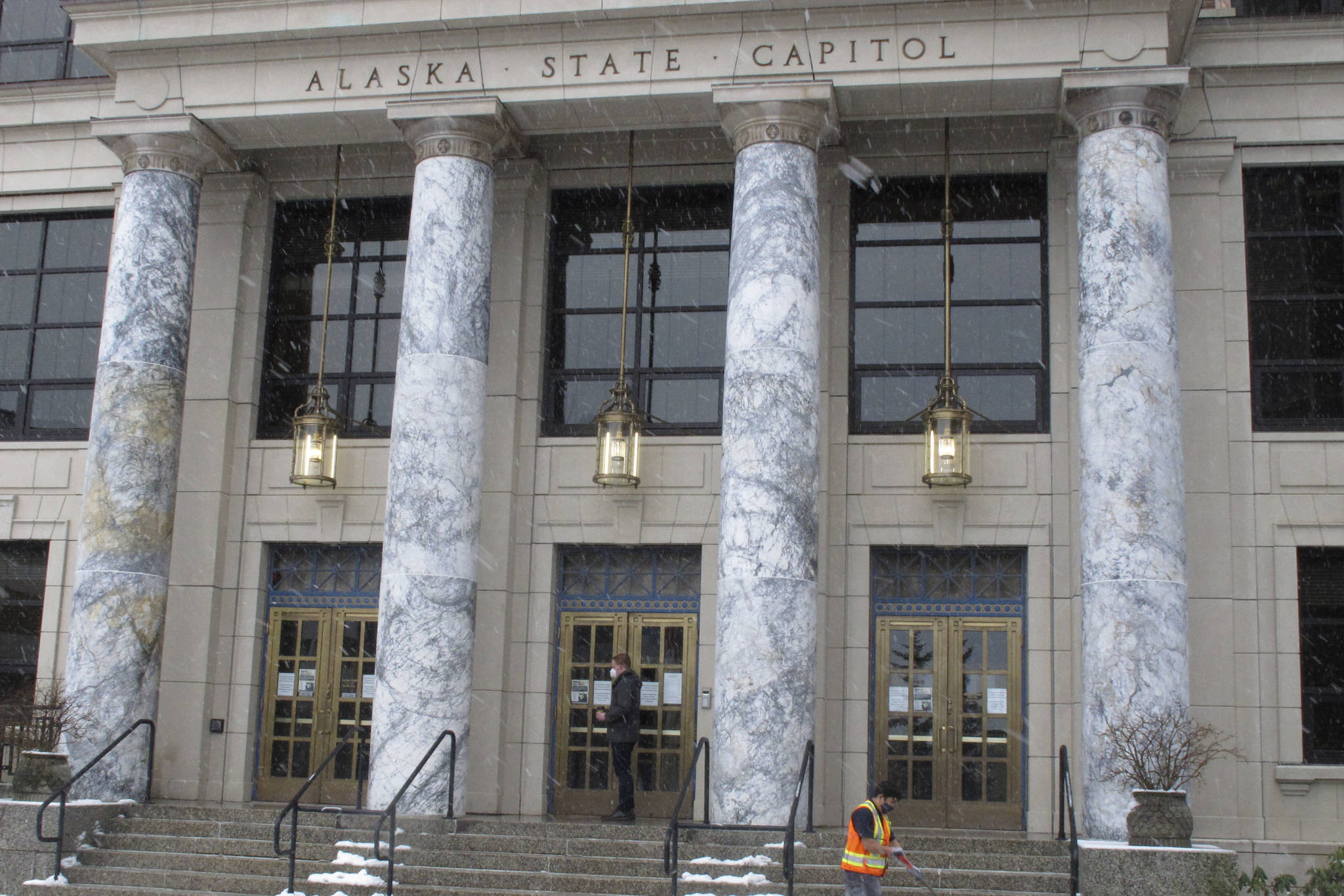 A legislative aide enters the Alaska State Capitol as a worker clears snow from in front of the building on Thursday, Feb. 25, 2021, in Juneau, Alaska. The Alaska House speaker announced on Wednesday, Feb. 24, that a House member had tested positive for COVID-19. (AP Photo/Becky Bohrer)