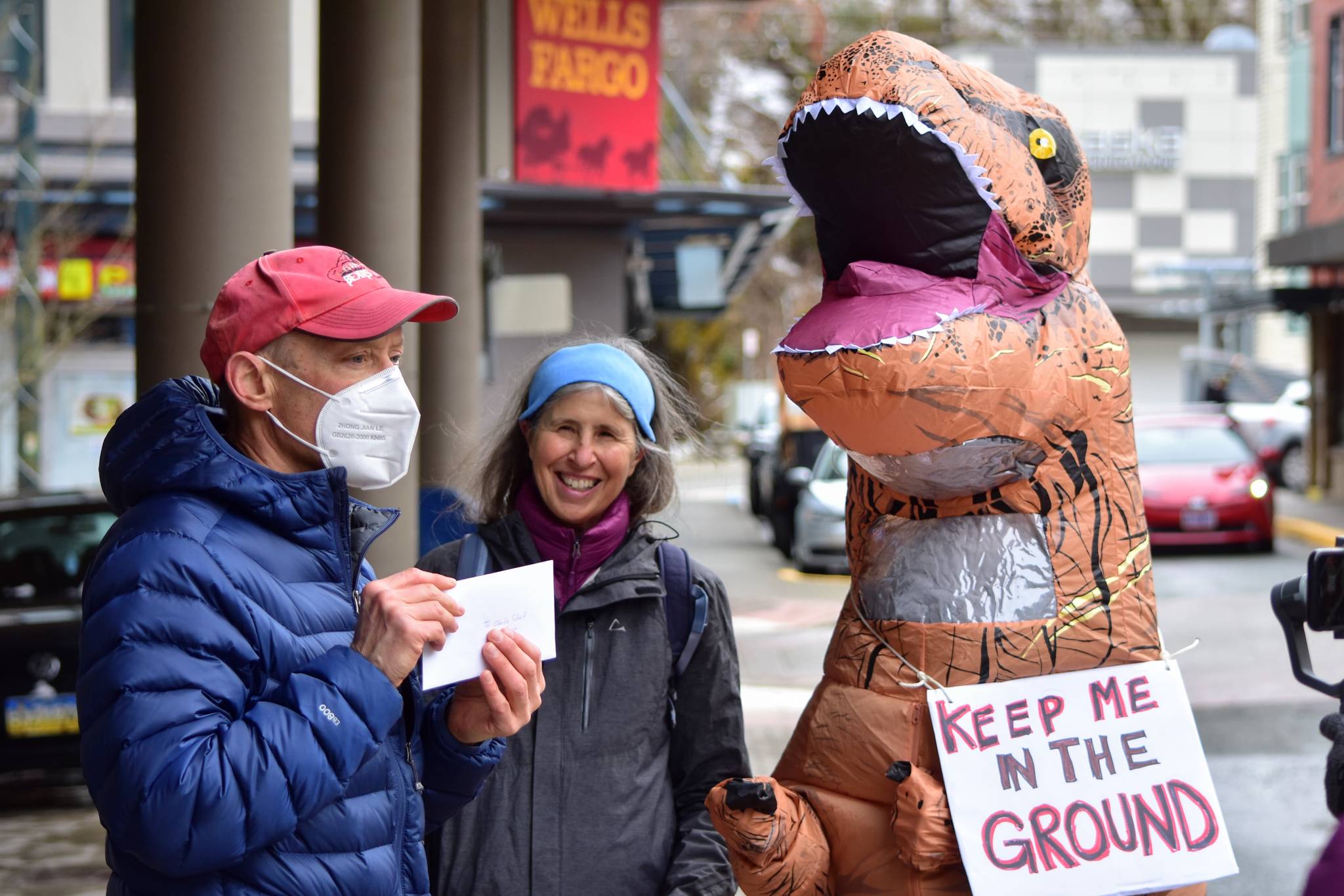 Peter Segall / Juneau Empire
Doug Woodby, co-chair of environmental group 350Juneau, holds up a letter addressed to the CEO of Wells Fargo alongside Irene Alexakos and Dick Farnell, wearing the costume. The group delivered the letter urging divestment from the fossil fuel industry to the bank’s branch in downtown Juneau on Friday, April 2, 2021.