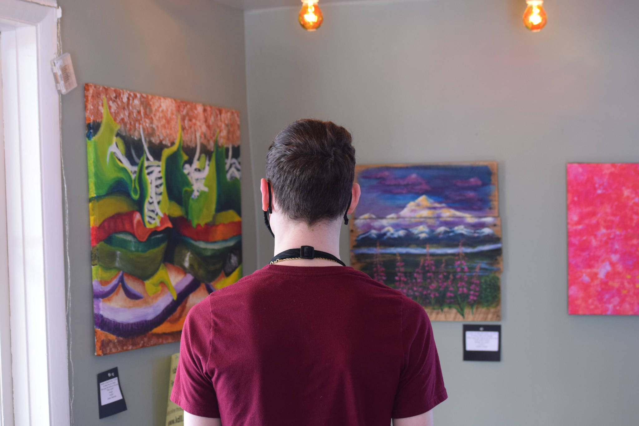 Samuel Anderson examines artwork up for bid while on shift at Veronica’s Cafe on April 7, 2021. The Kenai Fine Art Center and KDLL Public Radio are auctioning off local art through the month of April. (Photo by Camille Botello/Peninsula Clarion)