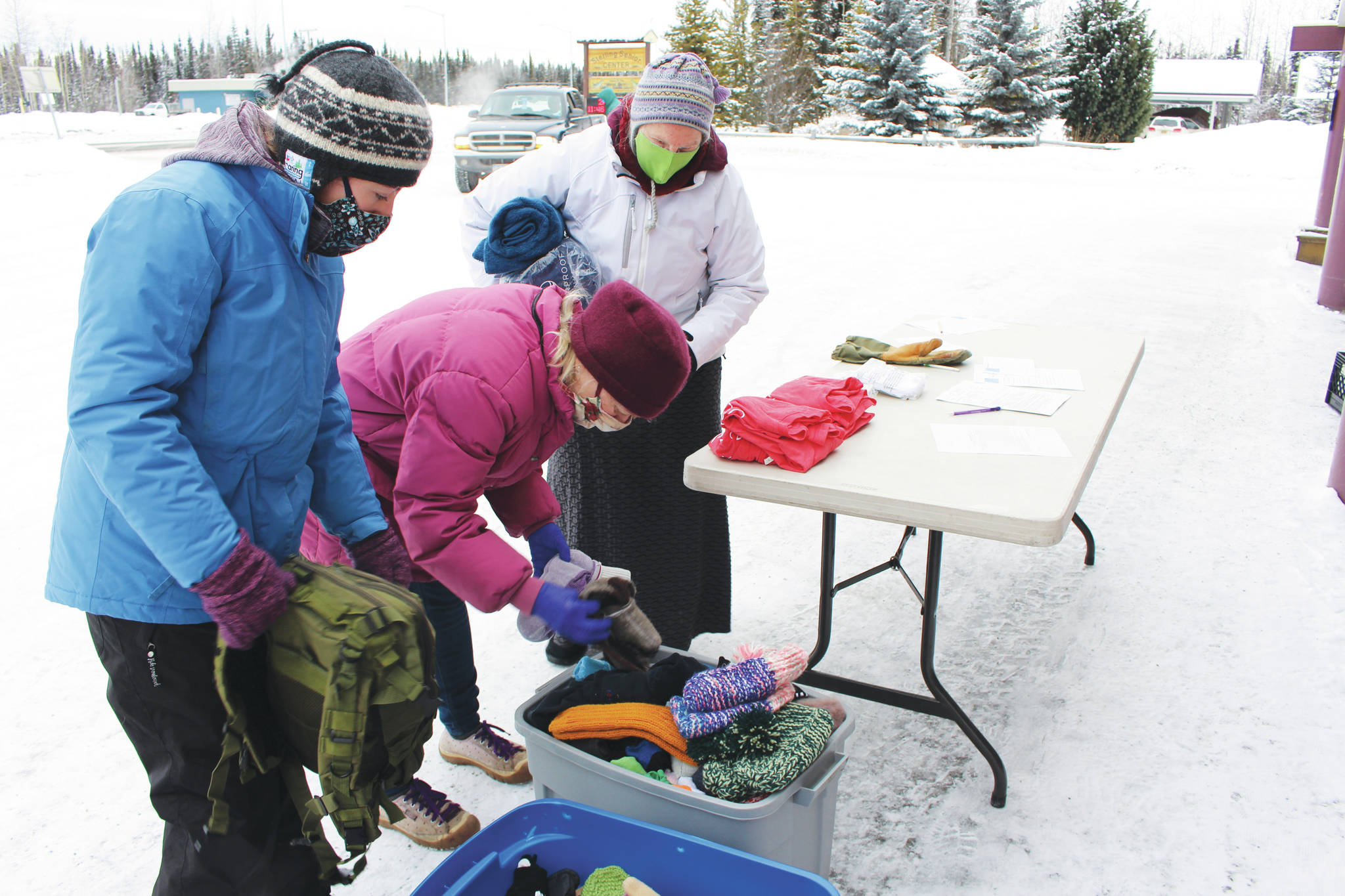 Project Homeless Connect volunteers help Arlene Jasky, center, pick out hats and gloves for a friend during a Project Homeless Connect event at the Sterling Senior Citizens Center in Sterling, Alaska on Feb. 2, 2021. (Photo by Brian Mazurek/Peninsula Clarion)