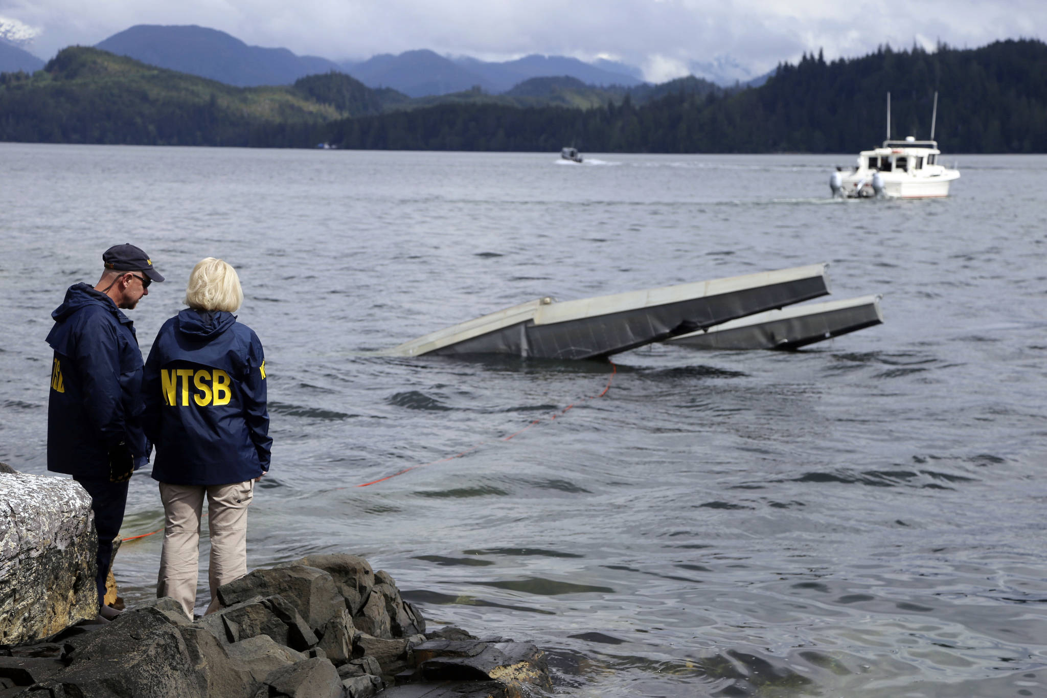 In this photo provided by the National Transportation Safety Board, NTSB investigator Clint Crookshanks, left, and member Jennifer Homendy stand near the site of some of the wreckage of the DHC-2 Beaver, Wednesday, May 15, 2019, that was involved in a midair collision near Ketchikan, Alaska, a couple of days earlier. The pilots of two Alaskan sightseeing planes that collided in midair couldn’t see the other aircraft because airplane structures or a passenger blocked their views, and they didn’t get electronic alerts about close aircraft because safety systems weren’t working properly. That’s what the staff of the National Transportation Safety board found in their investigation. (Peter Knudson/NTSB via AP)