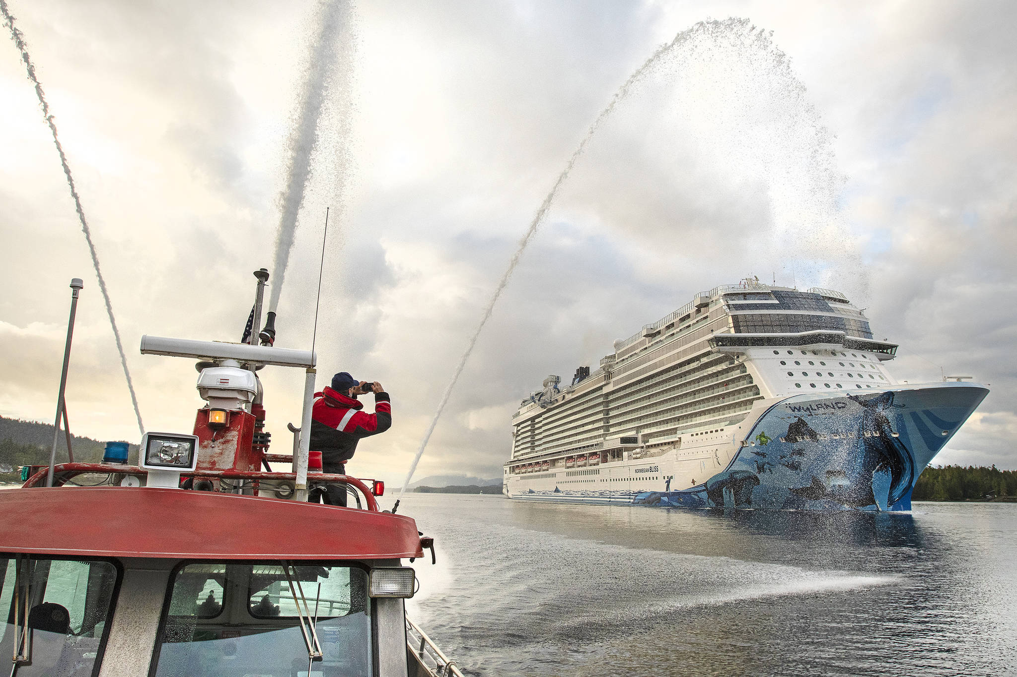 Firefighter medic Andy Tighe snaps a photo of the breakaway plus-class cruise ship Norwegian Bliss while Captain Tracy Mettler operates a fireboat in the Tongass Narrows in Ketchikan, Alaska, on June 4, 2018. President Joe Biden signed into law Monday, May 24, 2021, legislation that opens a door for resumed cruise ship travel to Alaska after the pandemic last year scrapped sailings. (Dustin Safranek/Ketchikan Daily News via AP)